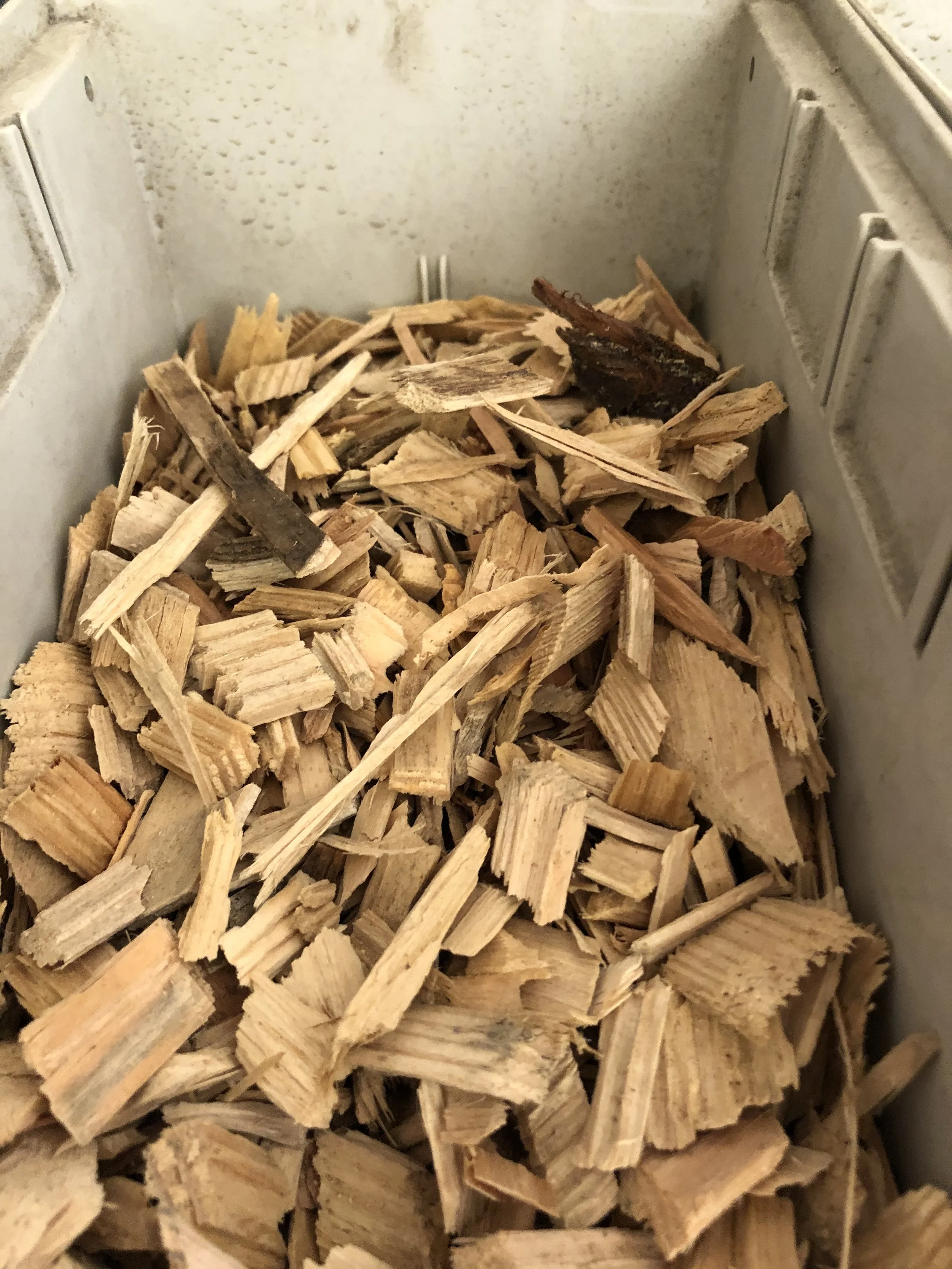 A metal storage container filled with small, irregularly shaped wood chips or kindling.