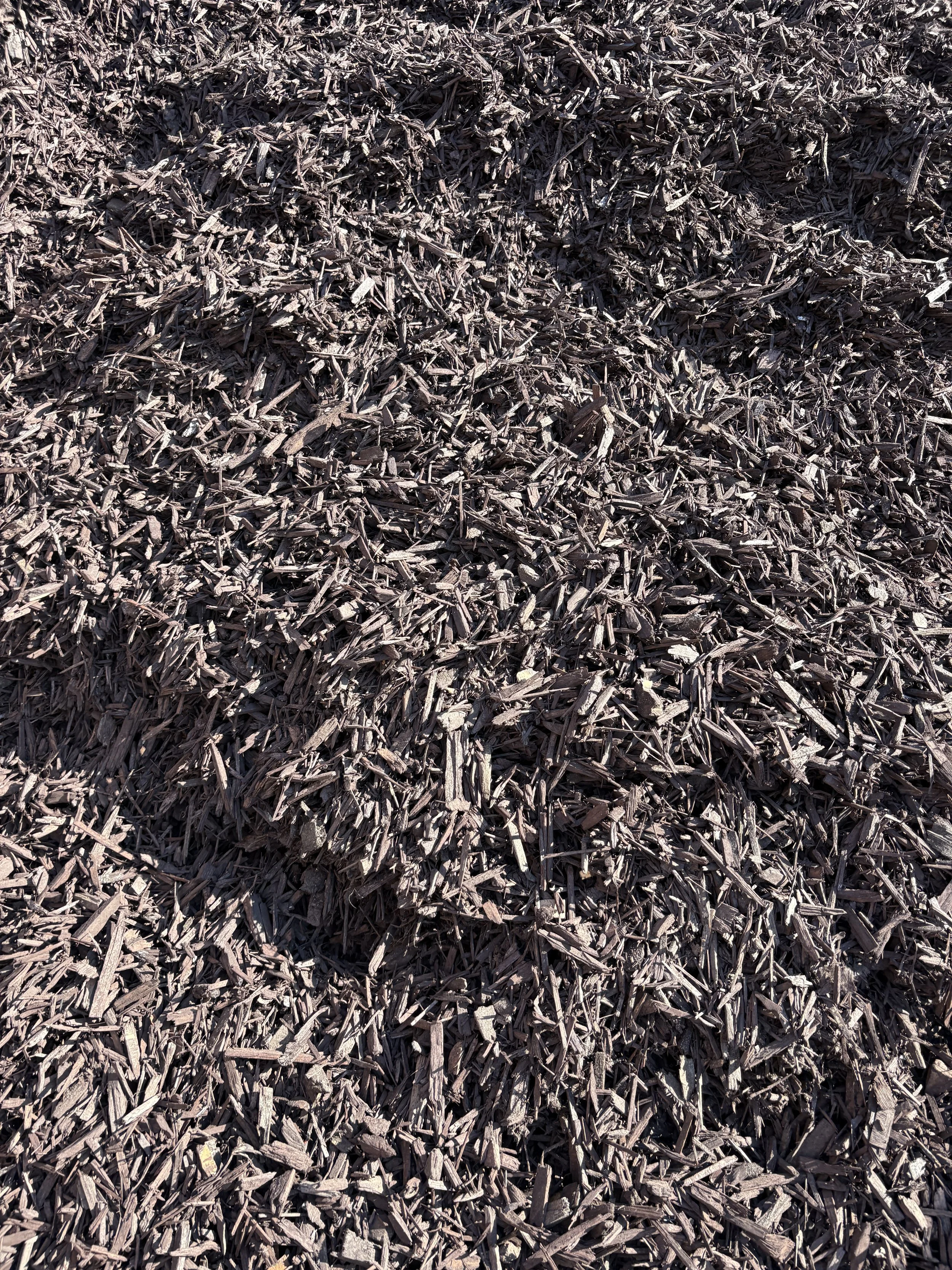 Close-up of a pile of shredded dark brown wood chips or mulch.