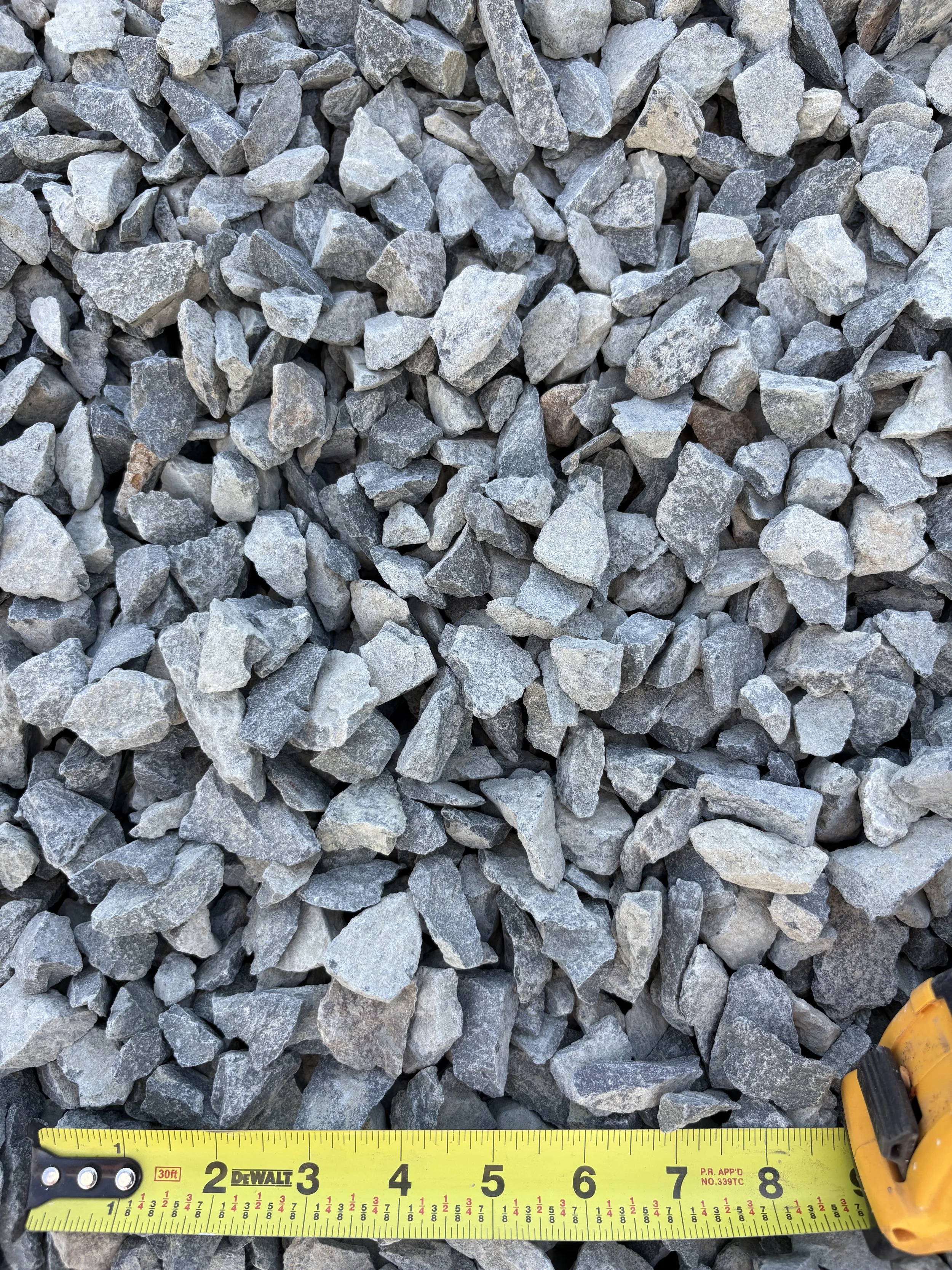 A close-up view of a pile of small gray rocks with a yellow measuring tape and a tape measure in the bottom right corner.