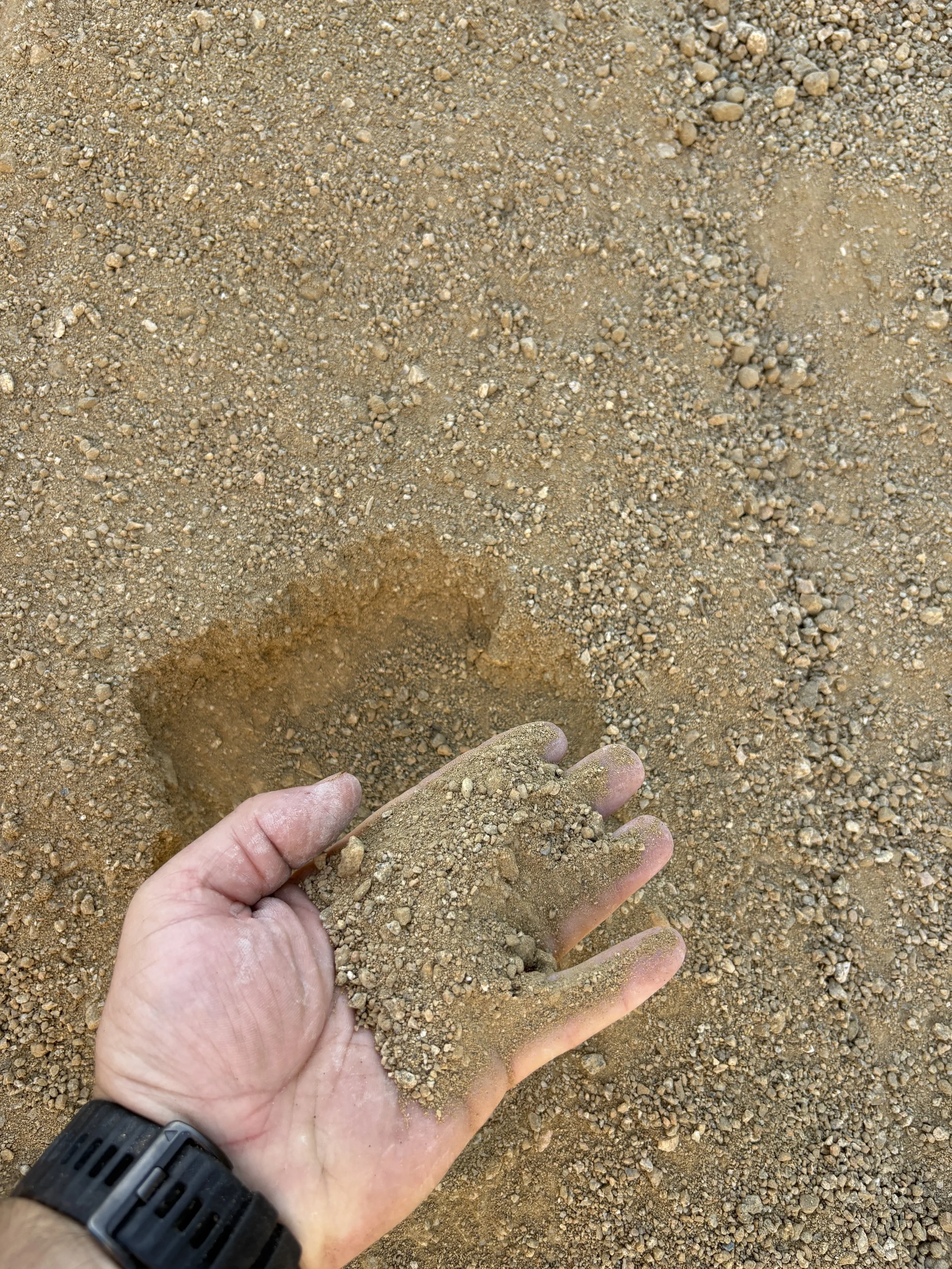 Person holding a handful of sand with an INFO hole in the ground in the background.