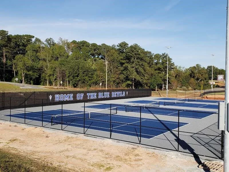 Blue tennis courts with a black printed Home of the Blue Devils windscreen