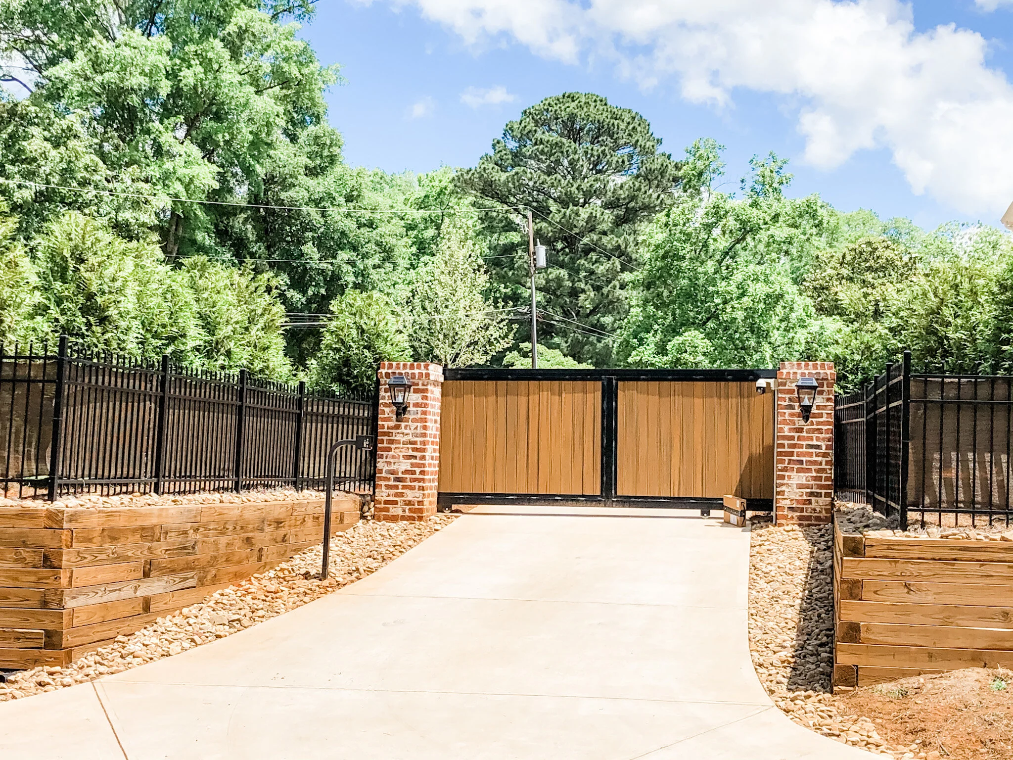 Custom ornamental metal and wood gate on brick columns with ornamental fence and windscreen.
