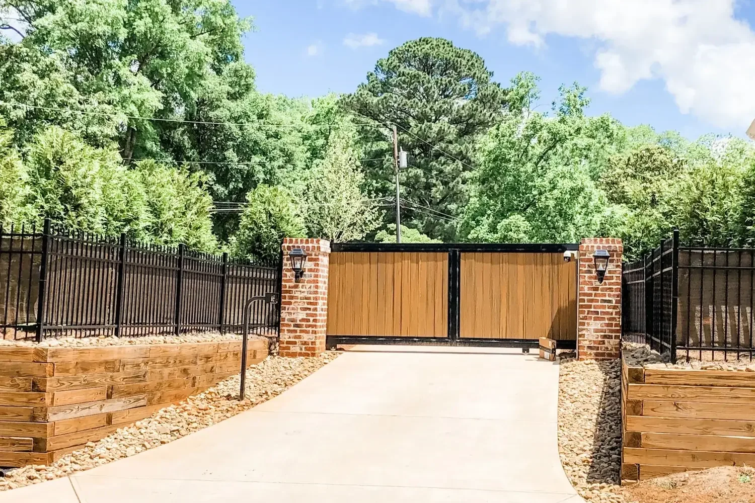 Wood driveway gate between brick columns with black metal fencing
