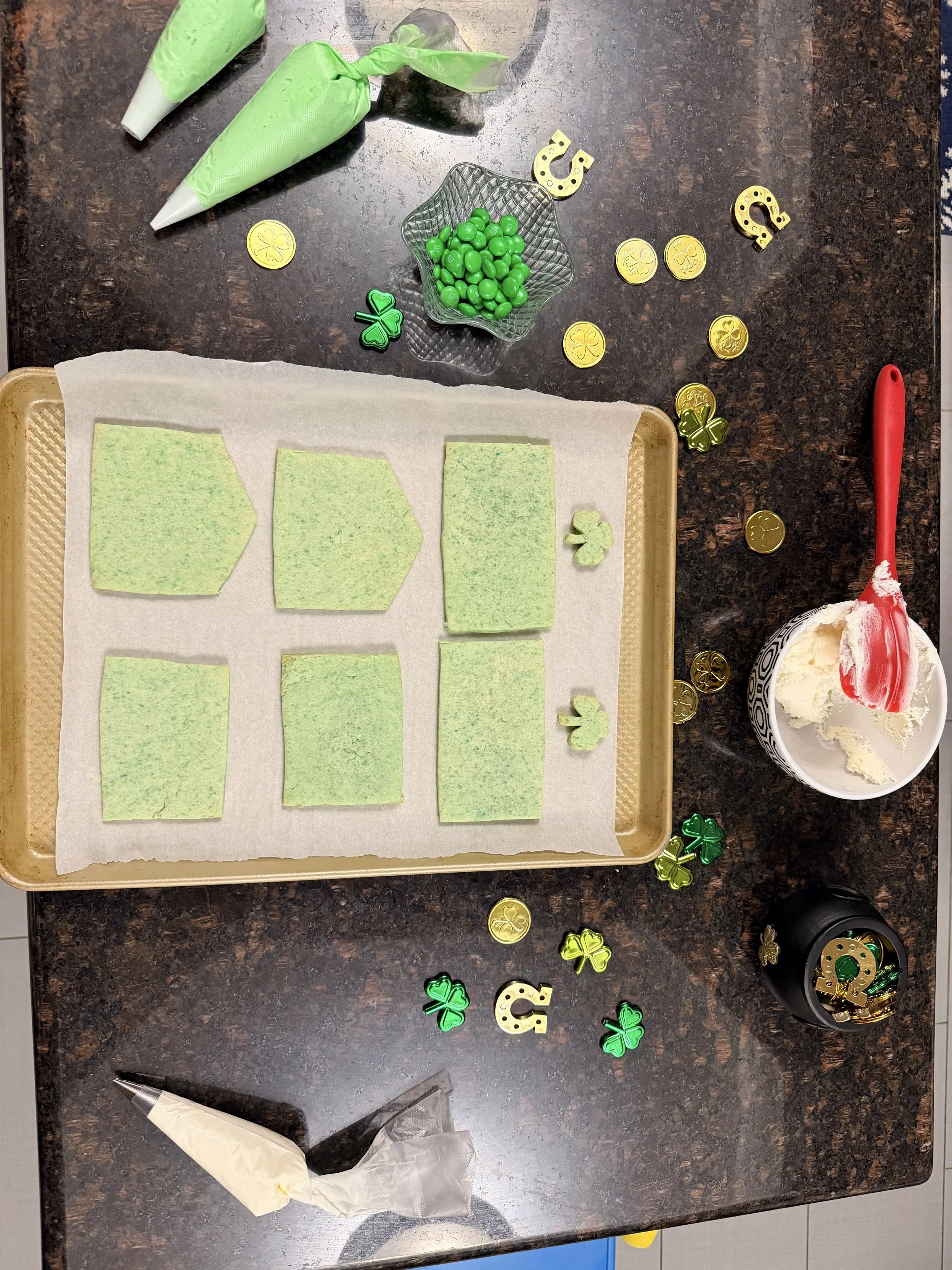 Green sugar cookie house panels baked and ready for assembly on a tray with buttercream icing and gold coins for a St. Patrick’s Day leprechaun trap.
