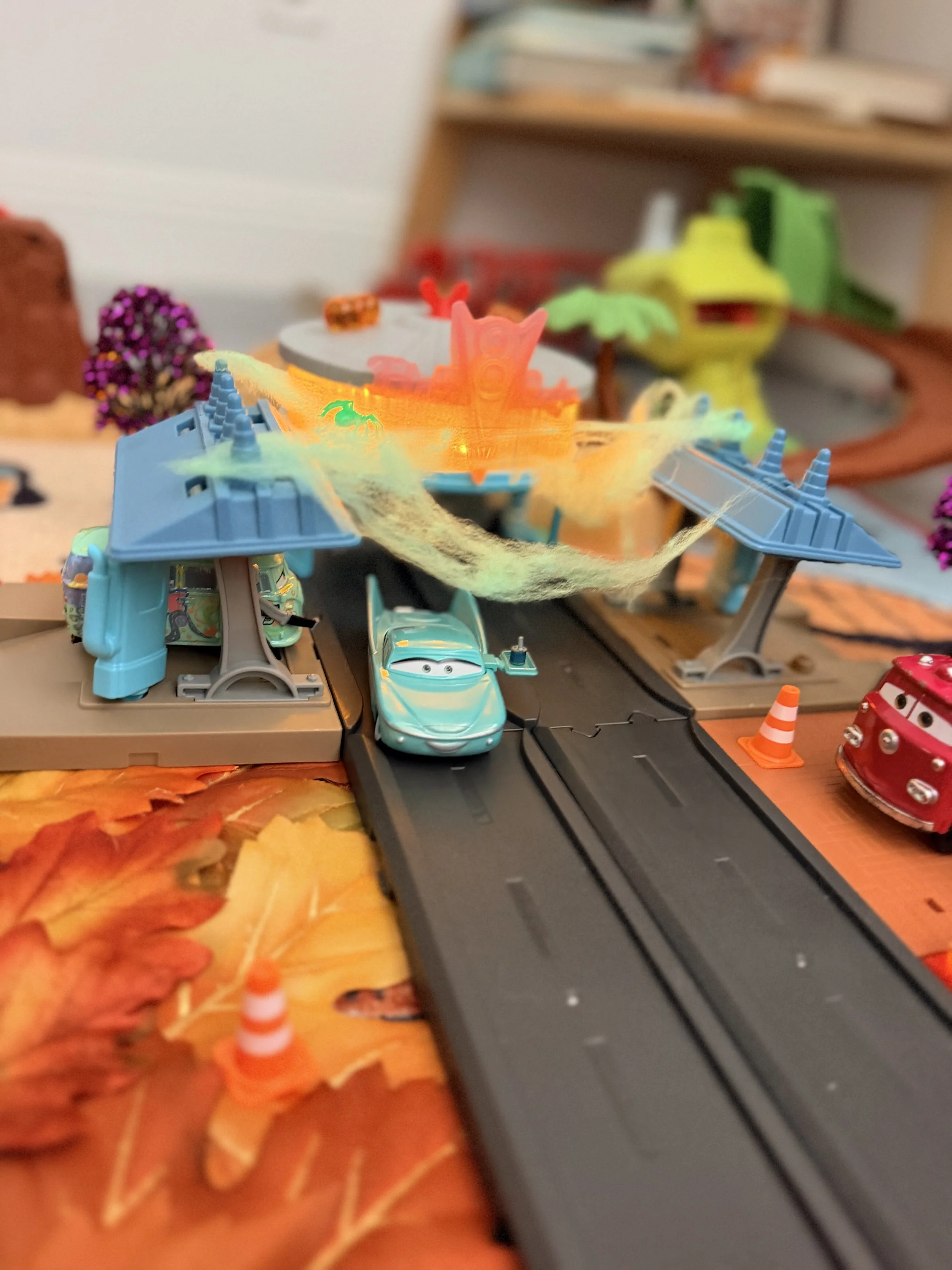 Cars Radiator Springs playset decorated for Halloween with stretched spiderwebs, orange lights, fall leaves and small Halloween decorations.