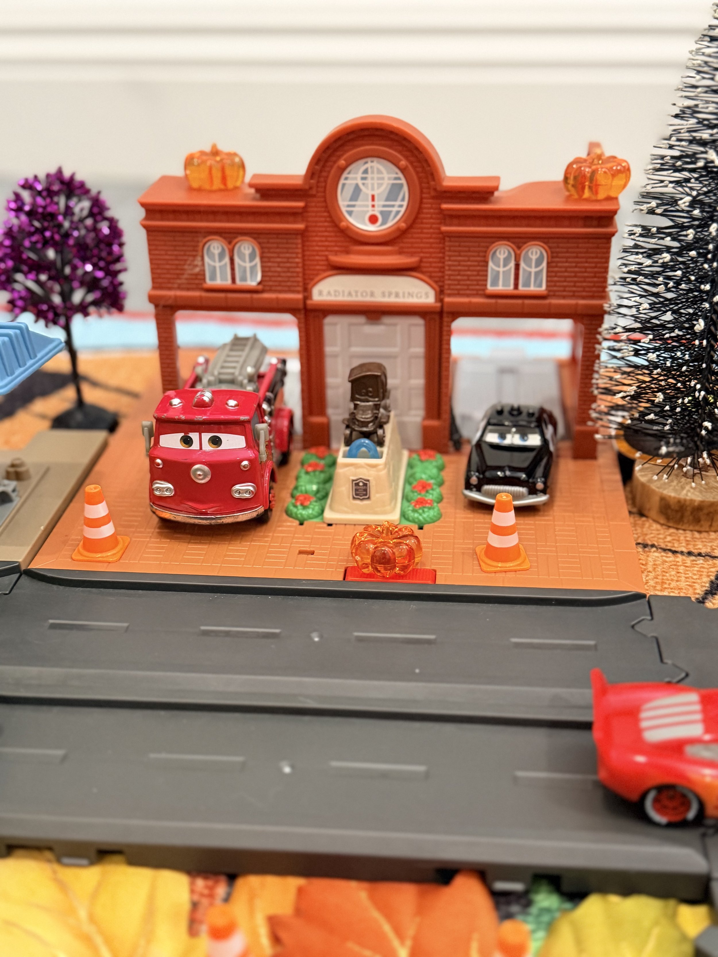 Radiator Springs fire station decorated with miniature pumpkins, Halloween trees and orange traffic cones for a Cars Halloween play activity.