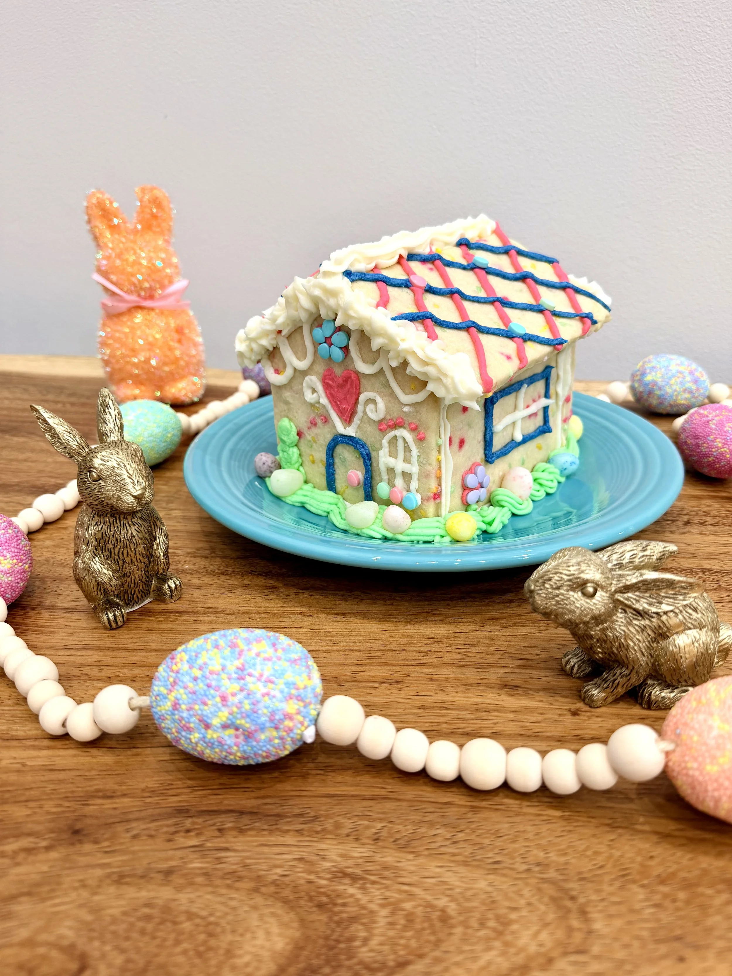 Easter Bunny Sugar cookie house with bunnies and eggs around it.