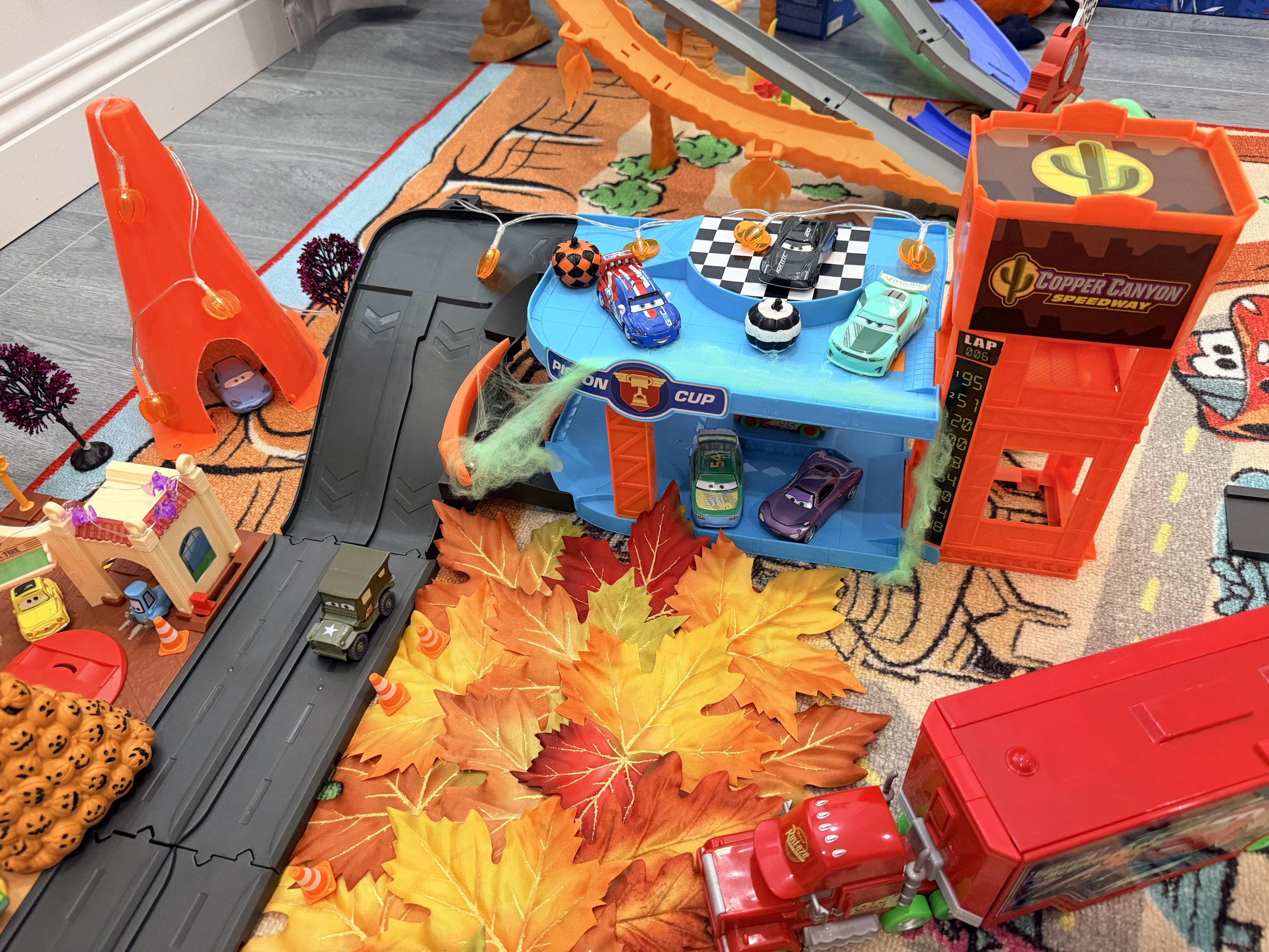 Overhead view of a Cars playset decorated for Halloween with colorful fall leaves, mini pumpkins, spiderwebs and seasonal decorations.