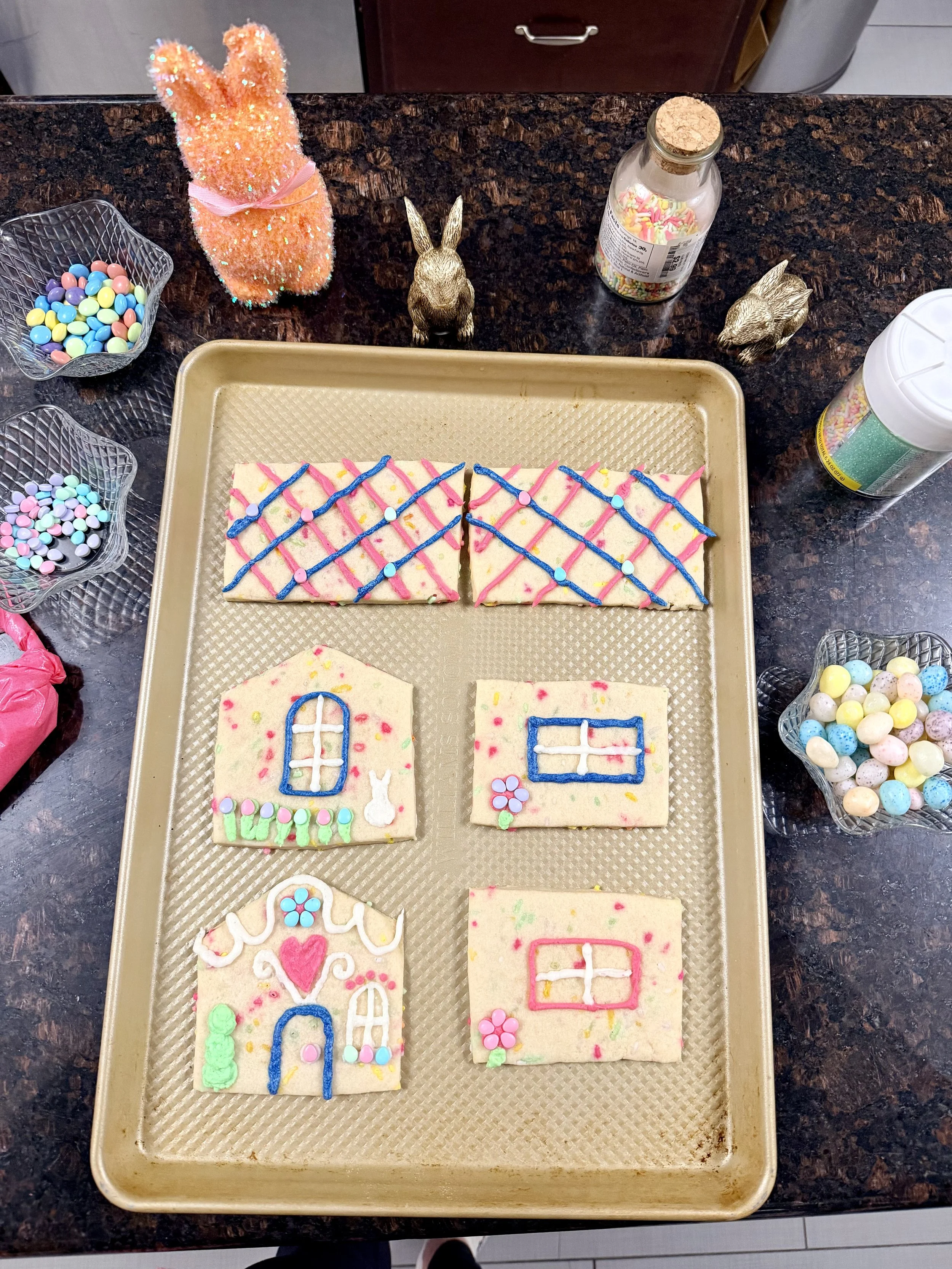 Sugar cookie house panels decorated with buttercream icing, pastel candy eggs, and piped details before assembly.