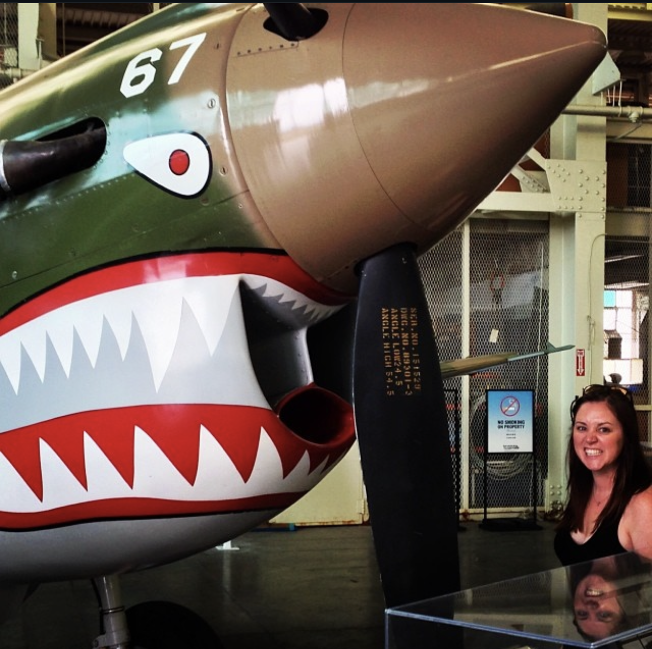 The author smiling in front of a vintage Curtiss P-40 Warhawk with shark-tooth nose art at the Pearl Harbor Aviation Museum in Oahu.