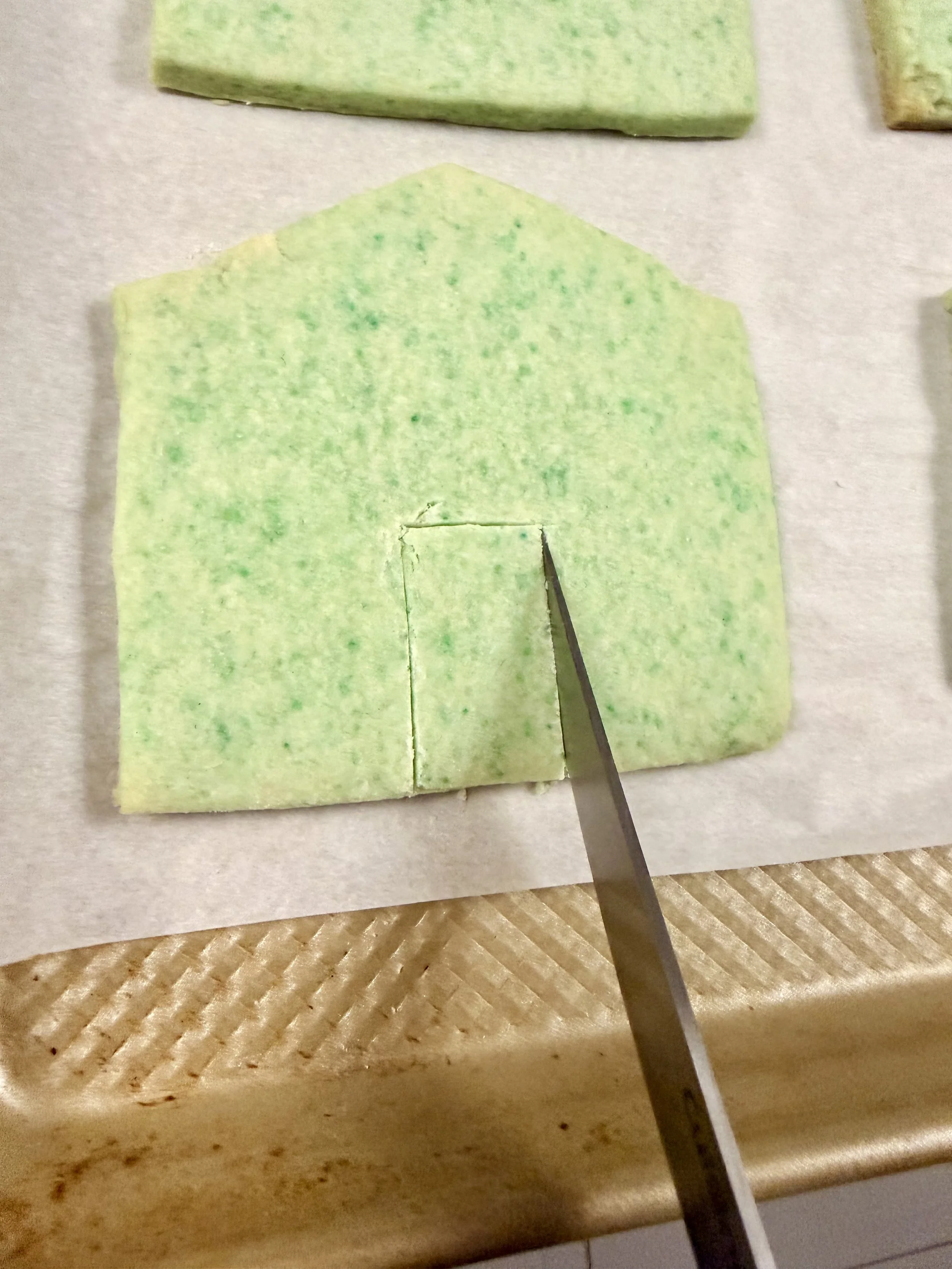 Cutting a front door into a sugar cookie house panel before baking for a St. Patrick’s Day leprechaun trap.
