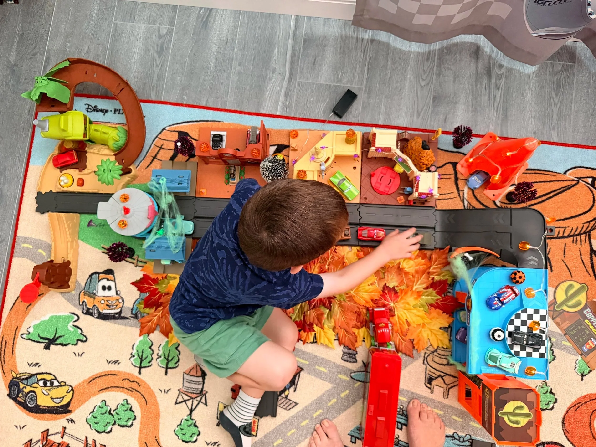 Preschooler playing with a Cars Radiator Springs playset decorated with fall leaves, pumpkins, lights and other kid-friendly Halloween decorations.