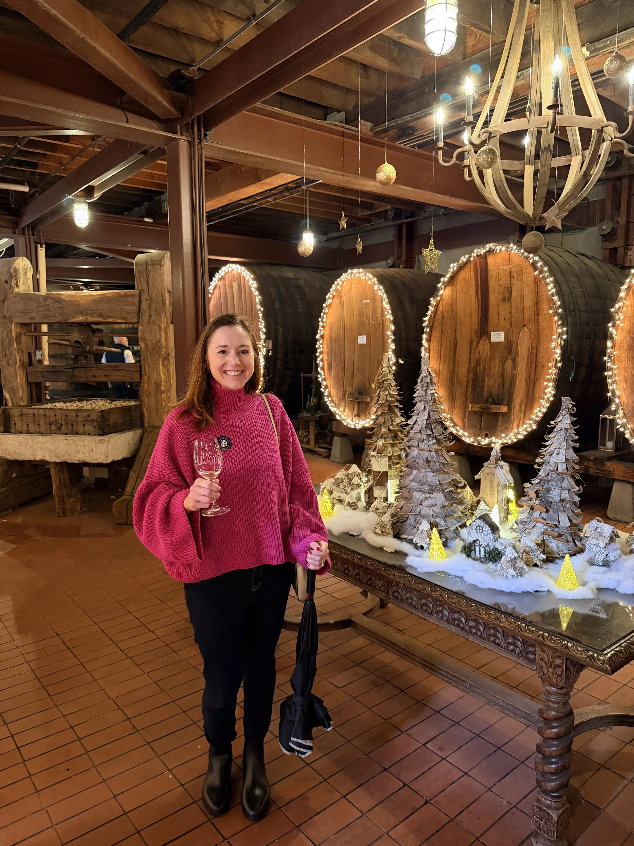 Pink Sweater, dark jeans, black rainboots, umbrella, gold crossbody bag outfit idea for wine tasting in Napa wine tour caves