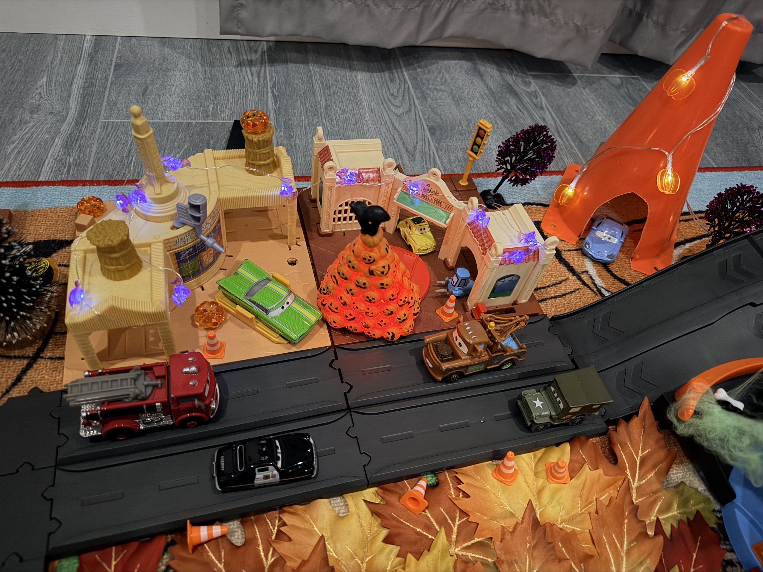 Halloween Cars playset decorated at night with pumpkin lights, purple lights, mini Halloween trees, fall leaves, Mater and other Cars characters.