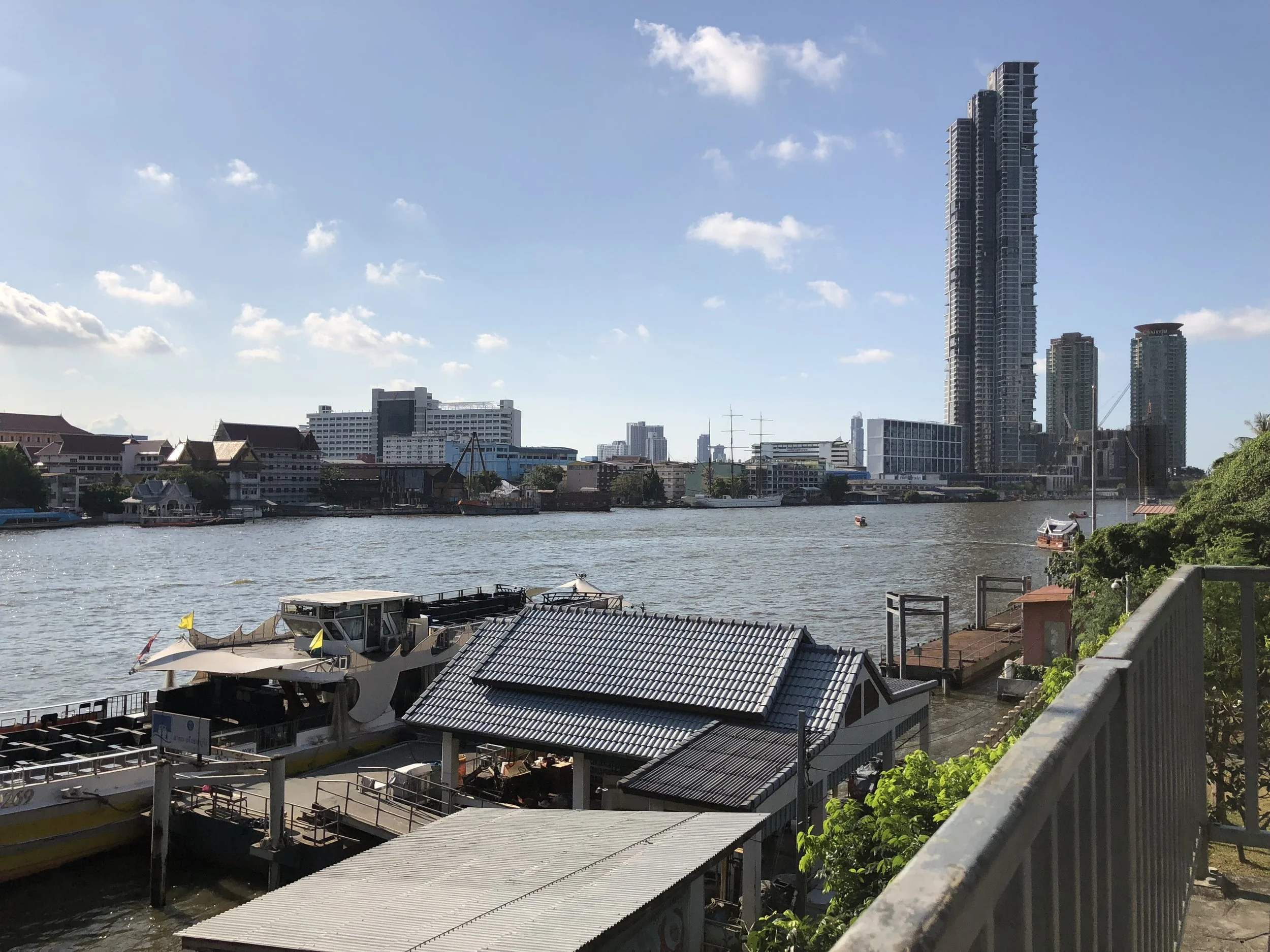 La vista de Chao Praya y un muelle con barcos para transportar la gente desde un puente.