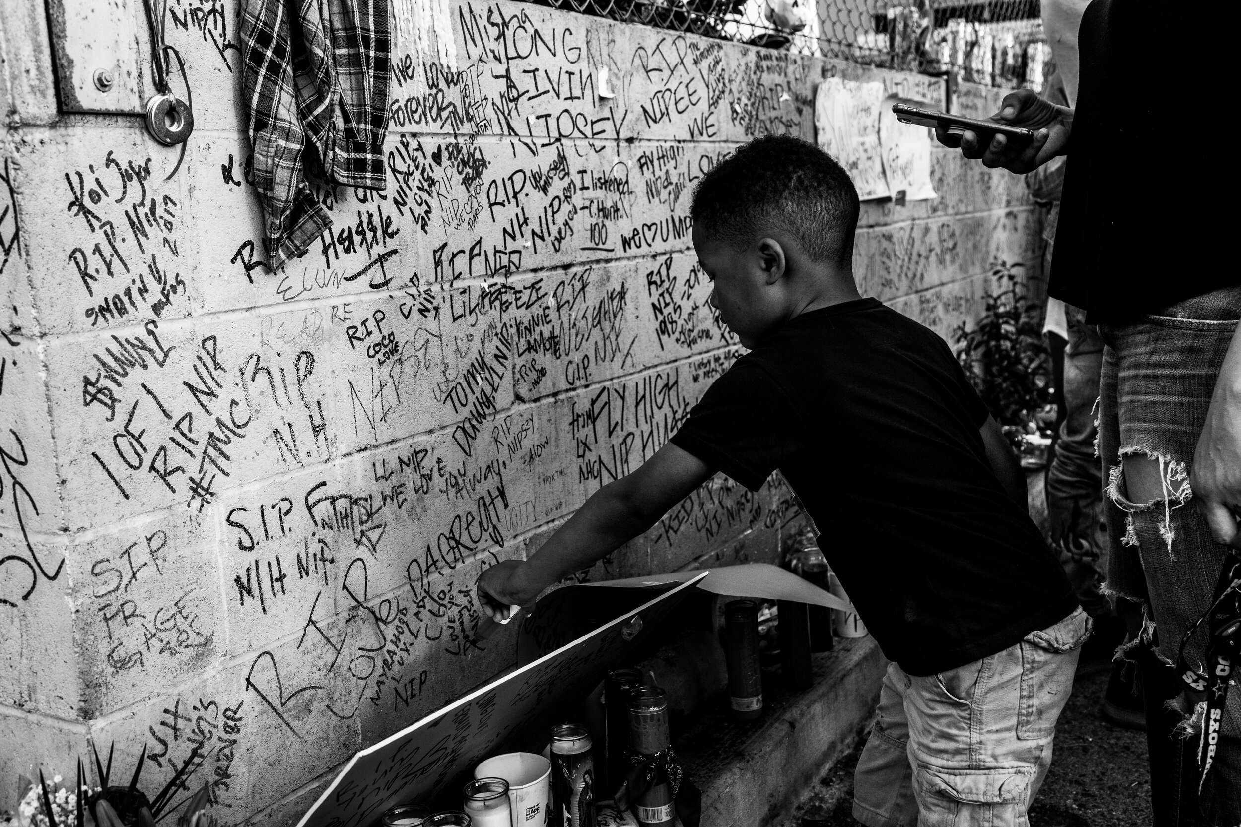  A young boy writes his farewell message to Nipsey Hussle on the wall in the alley next to the Marathon Clothing Store.  