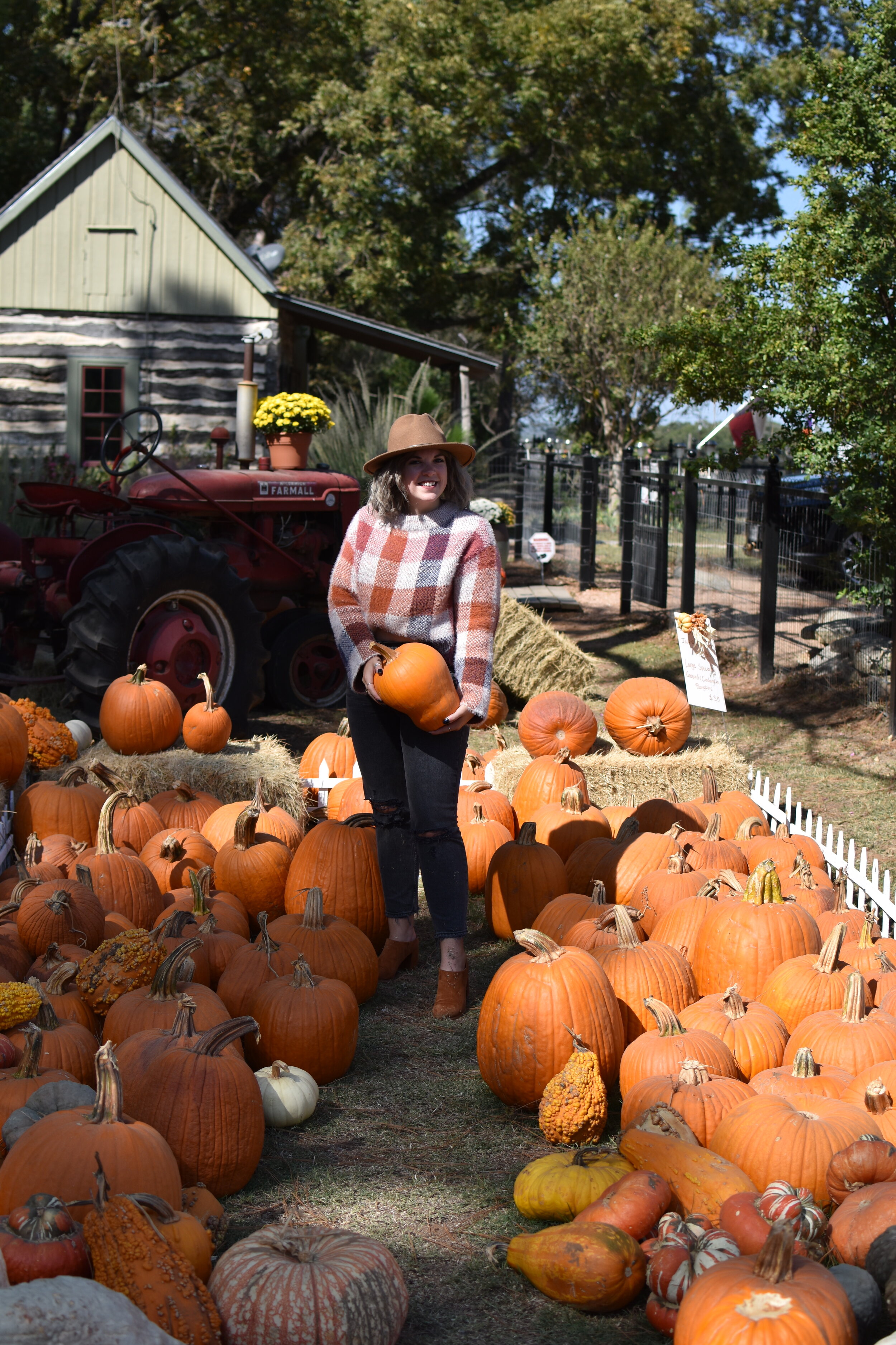 woman holding a pumpkin and surrounded by pumpkins on the floor