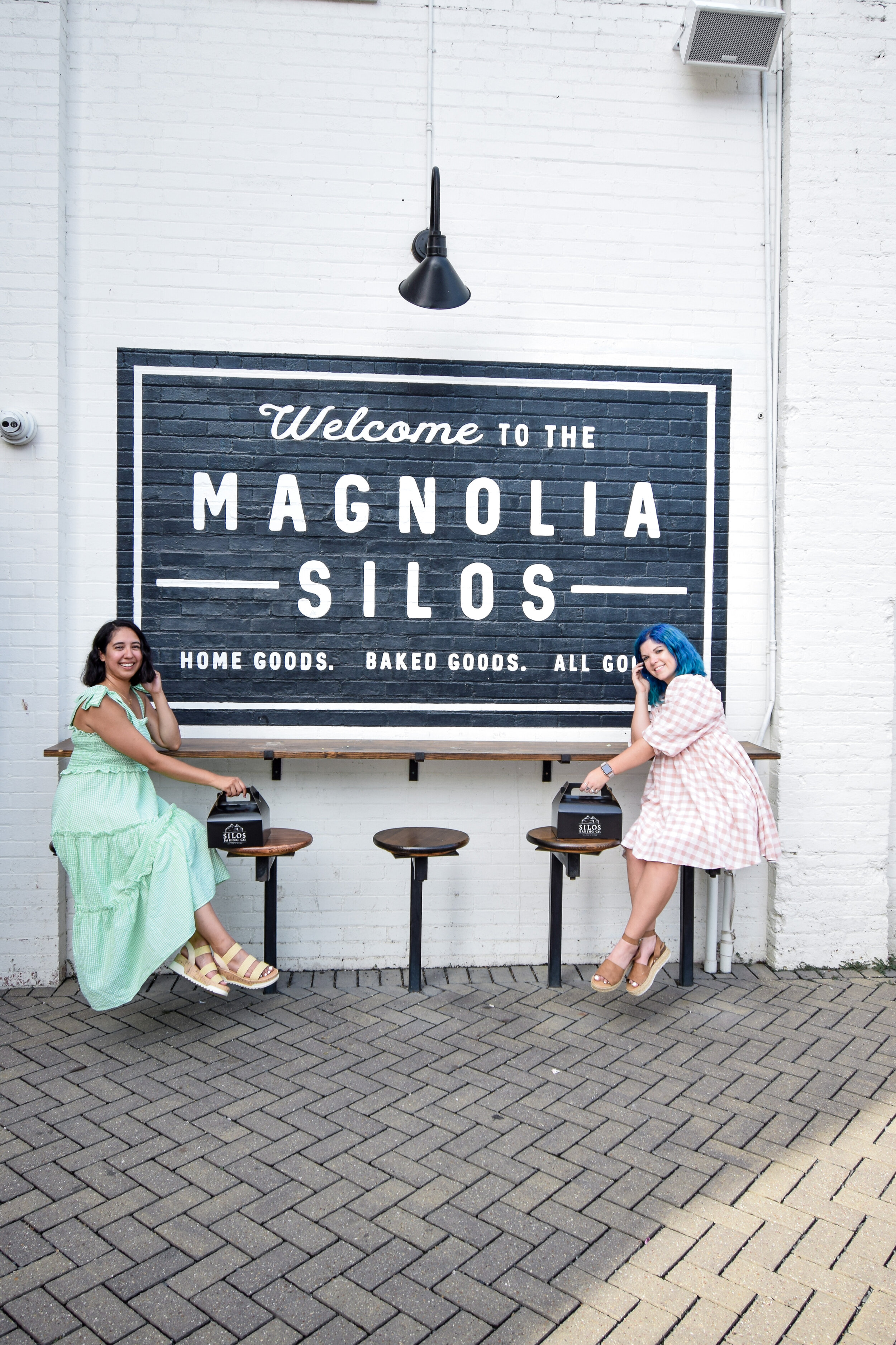 two women sitting behind the Welcome to the Magnolia Silos mural 
