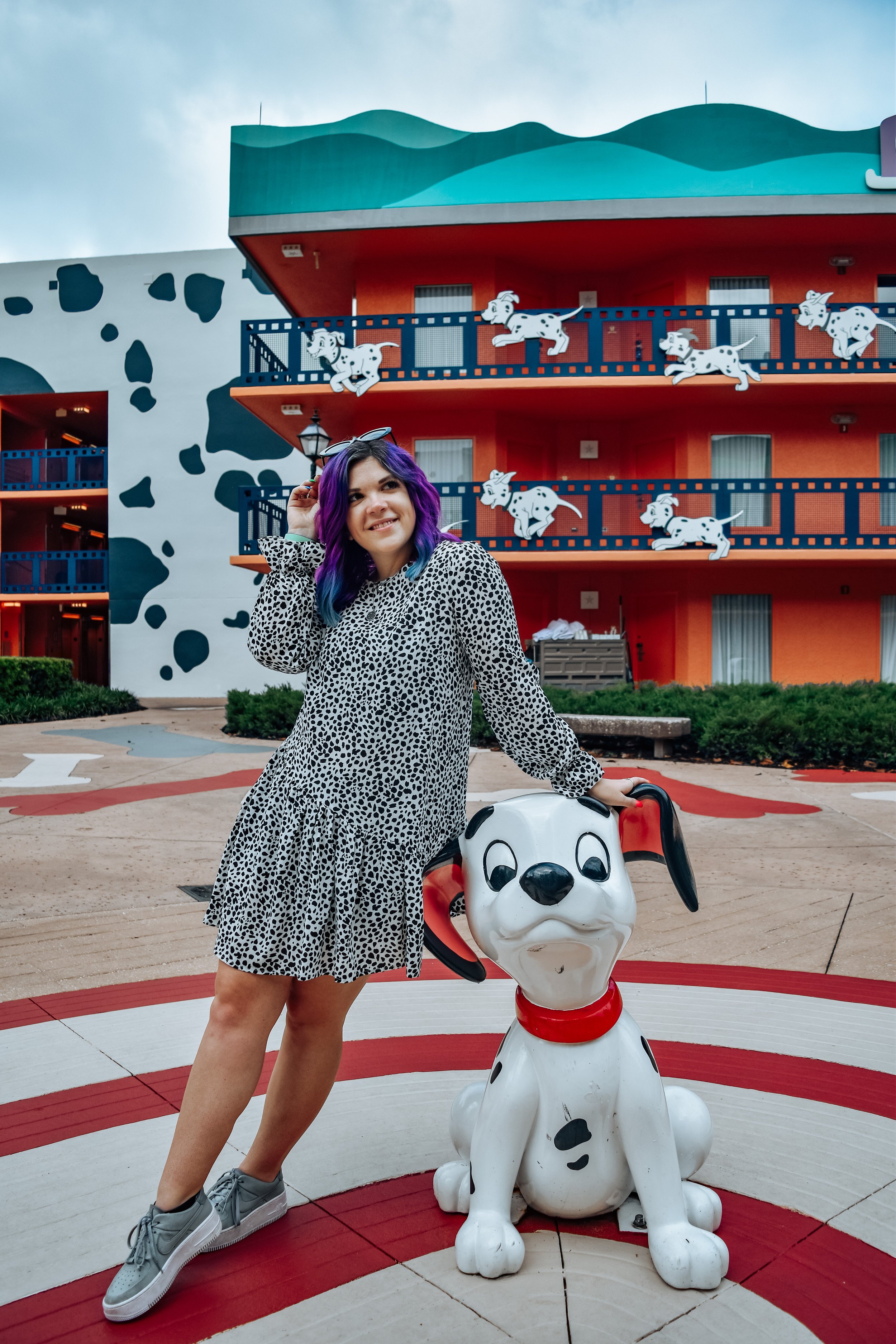 woman with purple hair leaning at a dog statue at disney's all-star movies resort