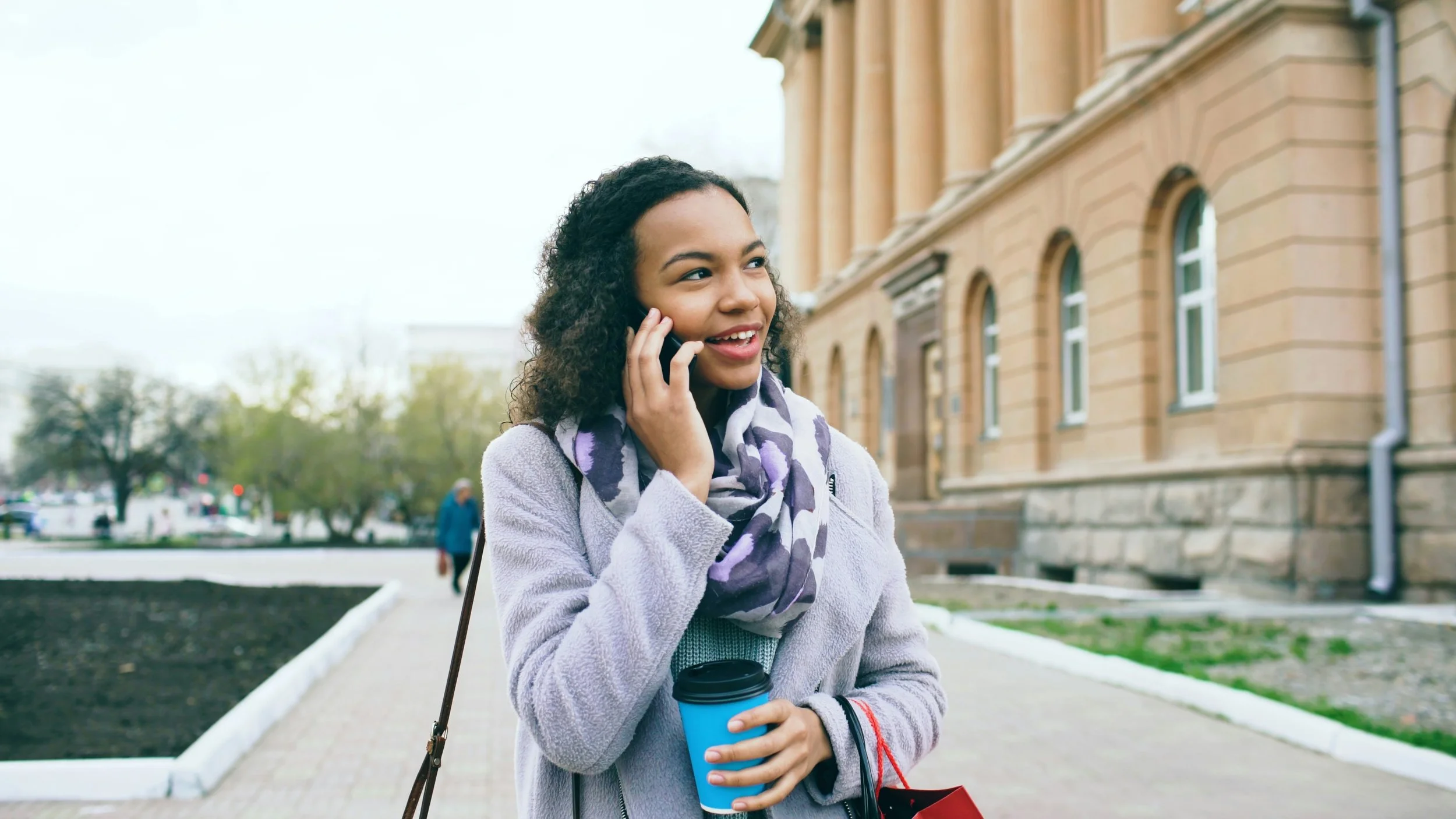 A college student on a phone call outside a campus building, arranging a free counseling consultation in Austin