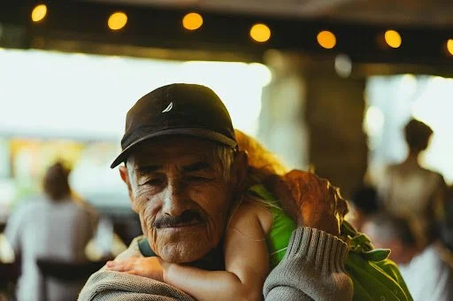 Elderly Latino grandfather smiling as his grandchild hugs him, reflecting the close family bonds valued in the Latino community