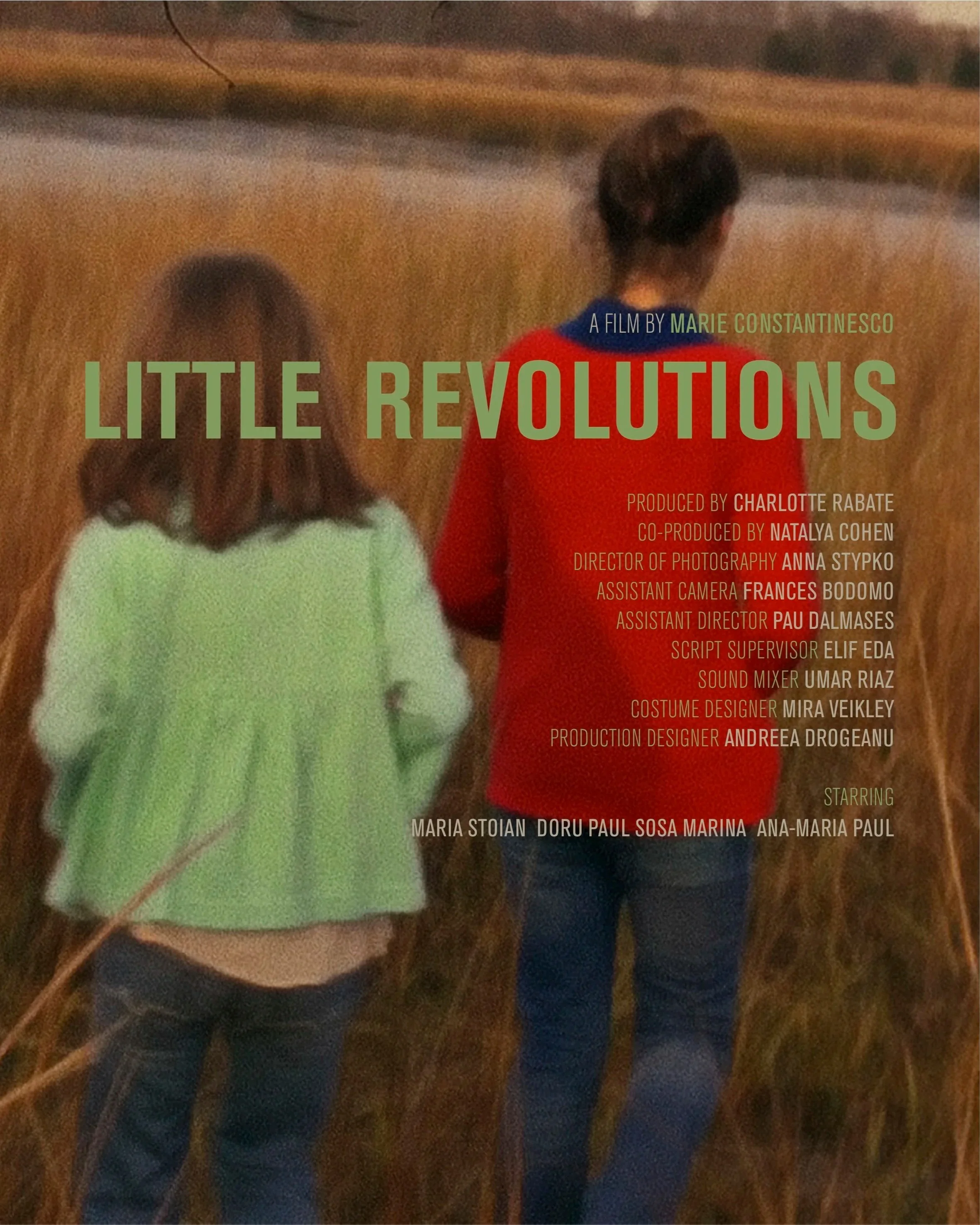 Two children, a girl with brown hair wearing a light green sweater, and a girl with dark hair wearing a red jacket, standing in a field of tall, dry grass during sunset. Super 16mm film