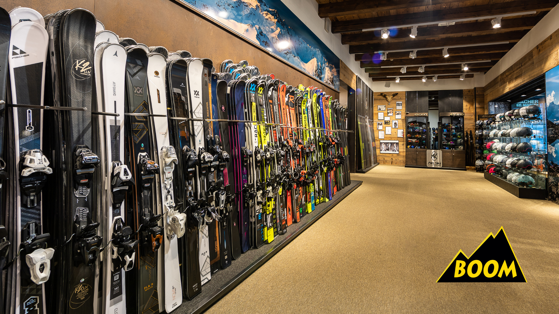 Skier in einem Sportgeschäft, das Skier, Skistiefel und Helme auf Regalen präsentiert, mit Bergbildern an der Wand.