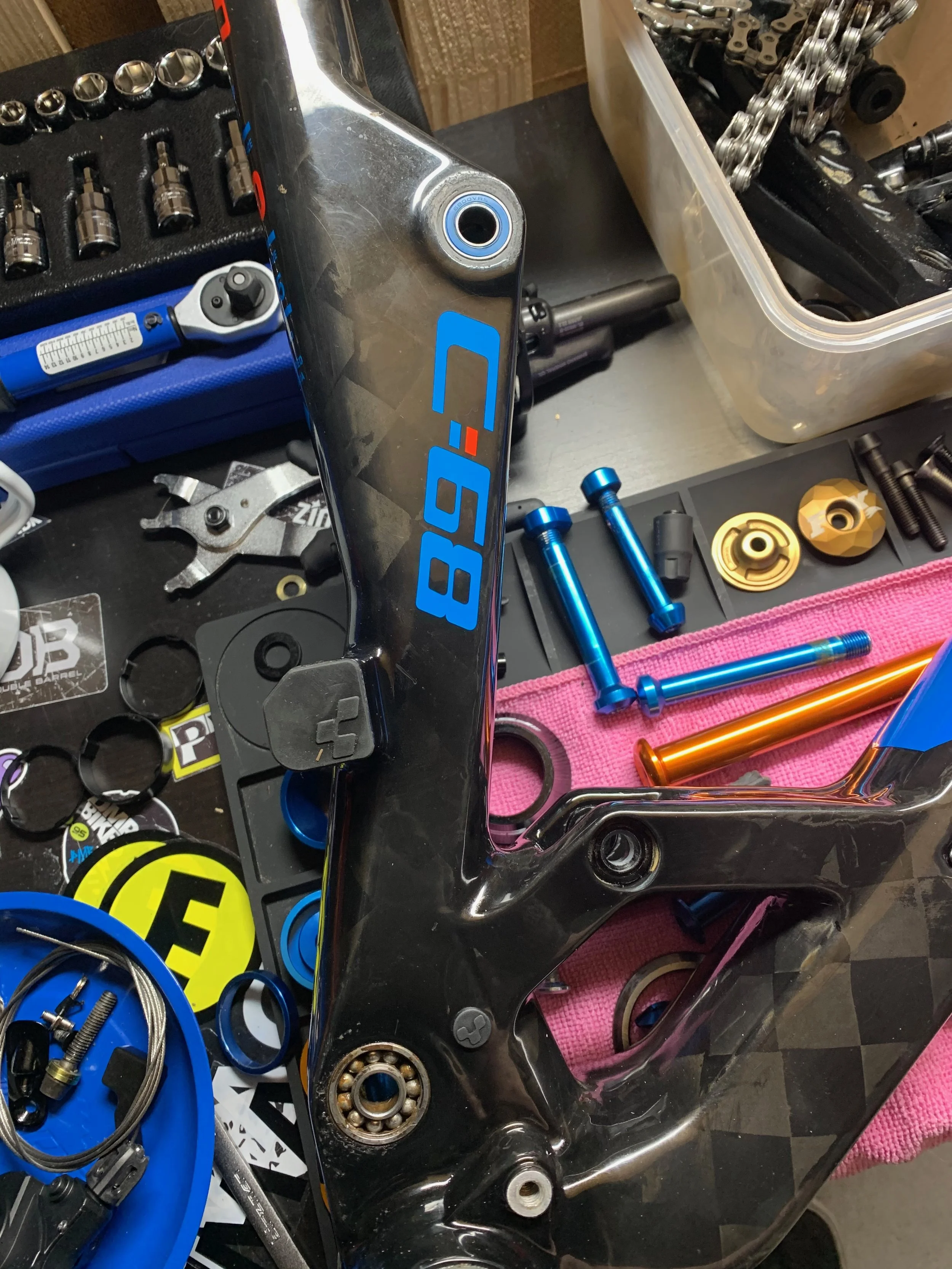 Officina con parti di biciclette, chiavi inglesi, cuscinetti a sfera, cavi, attrezzi e viti colorate sparse su un tavolo da lavoro.