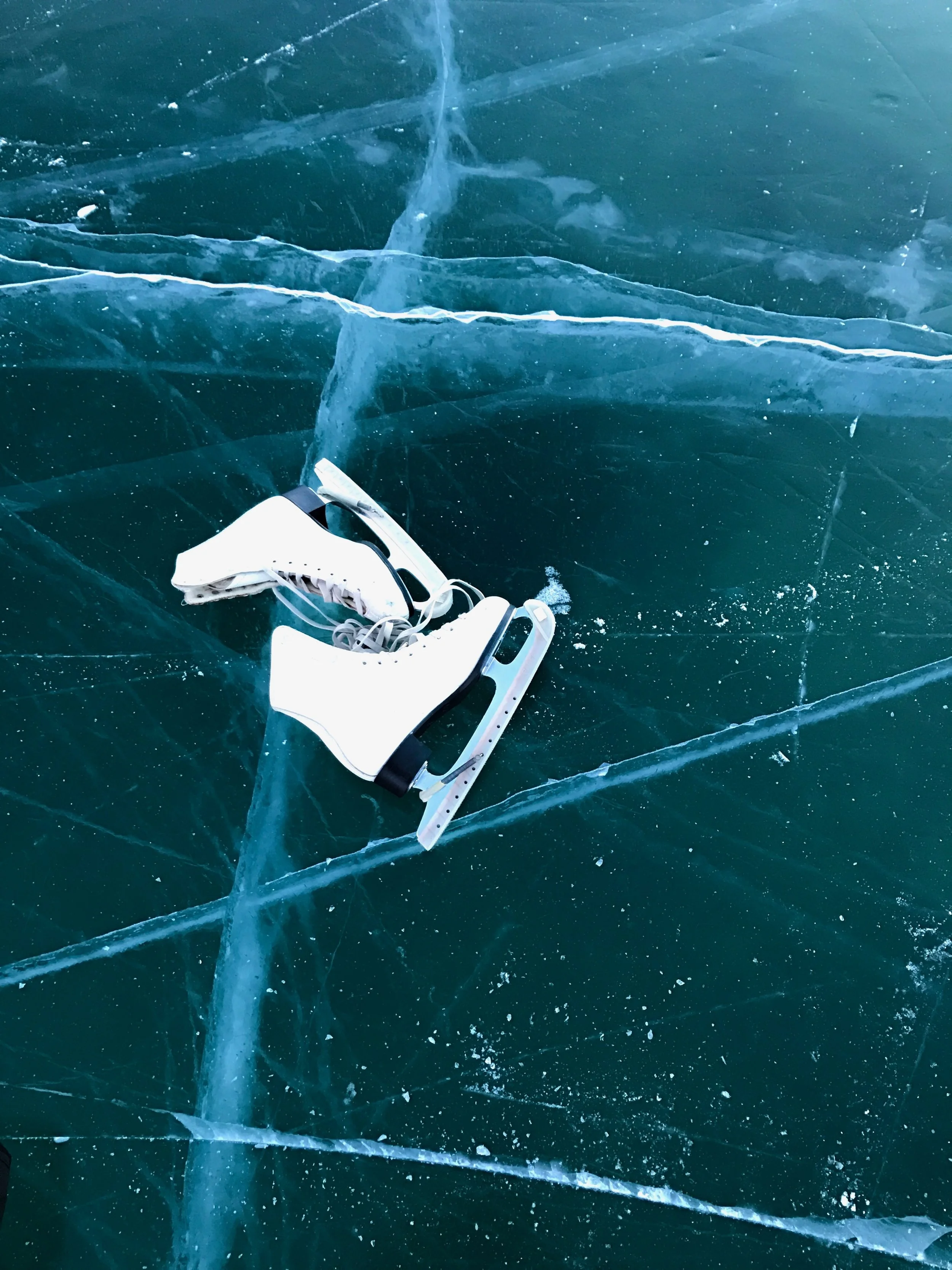On the ice lie a hockey stick and a hockey stick, resting on a frozen surface with visible cracks and bubbles in the ice.