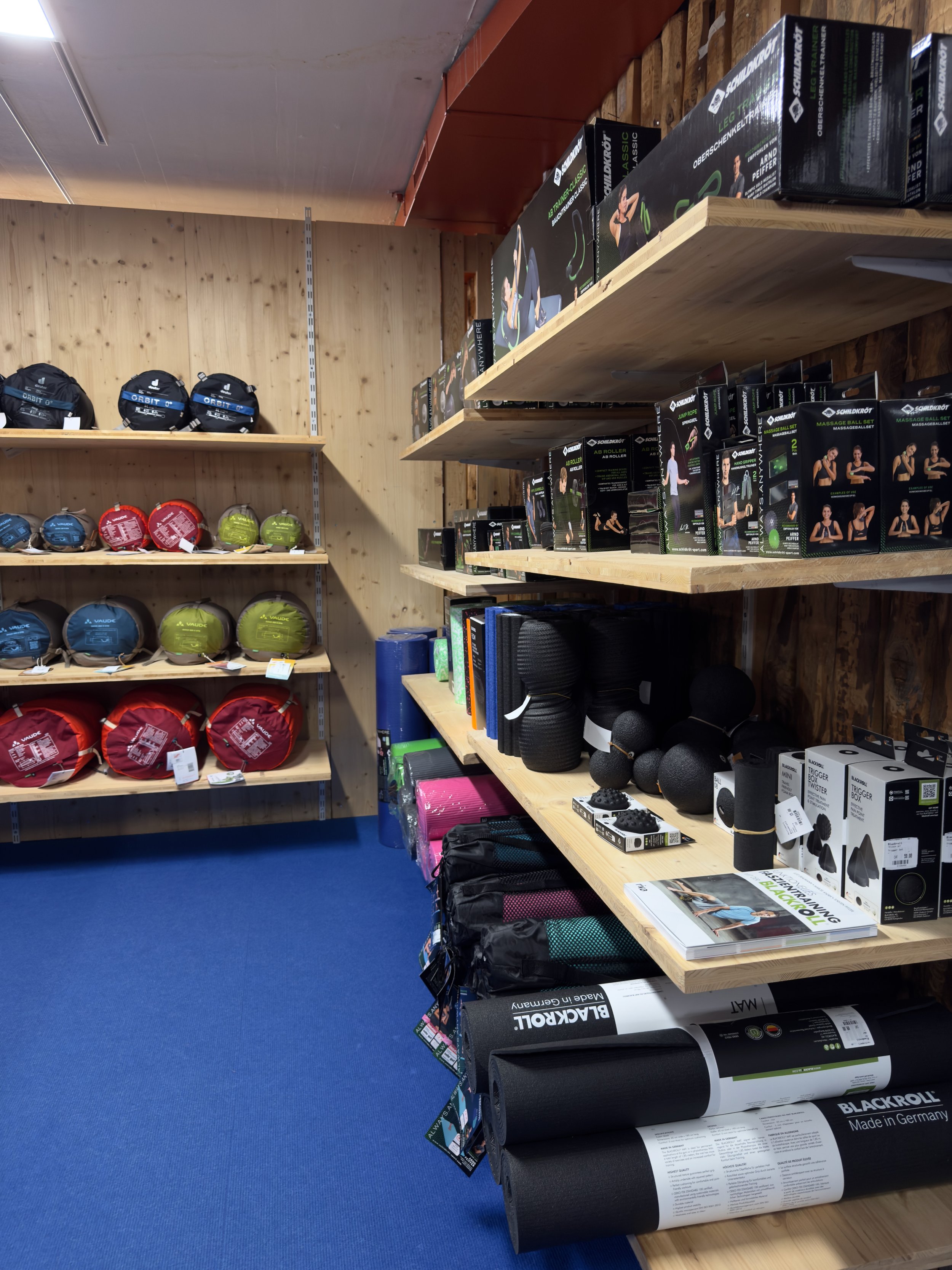 Shelves in a sports store displaying red, blue, green, and black yoga balls, fitness mats, and accessories.
