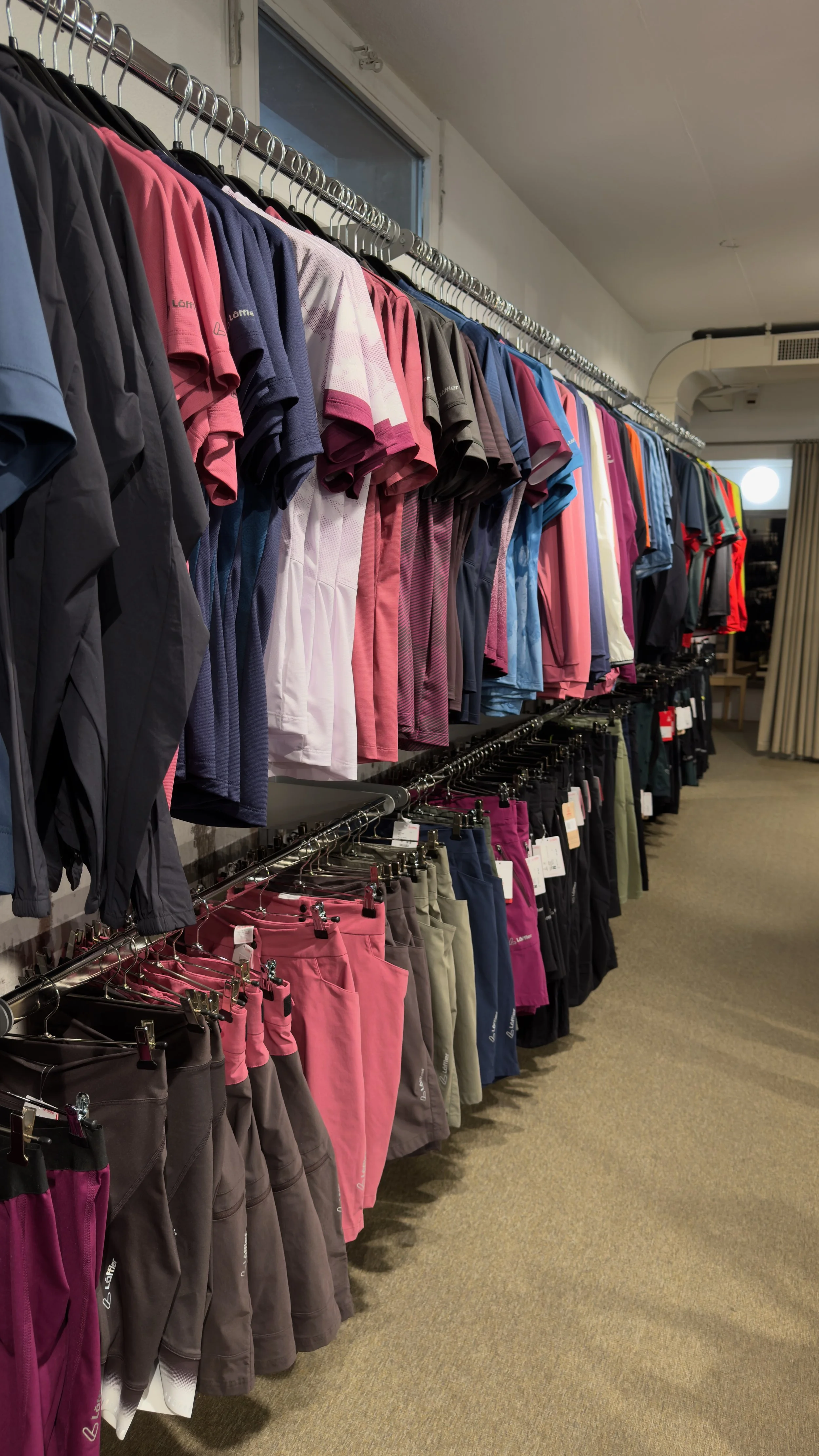 A view of a clothes rack displaying sportswear in various colors, including T-shirts, pants, and jackets, in a store.