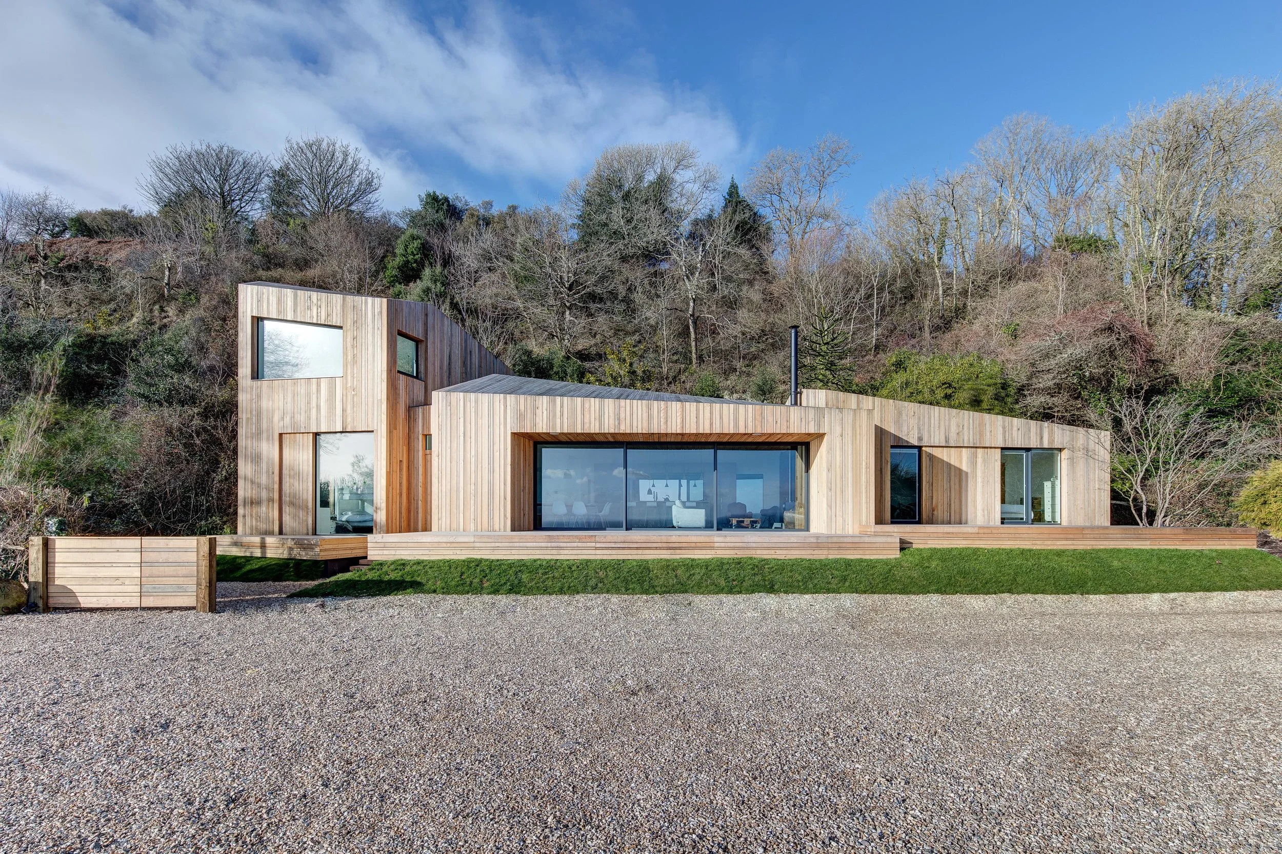 AR Design Studio was approached by the clients who were looking to extend their holiday home on a cliff top on the South Coast. During the planning process, and following the unprecedented rainfall during the winter of 2014, there was subsidence close to the house and the decision was made to replace it entirely. AR Design Studio was then tasked with designing a completely new home; the idea of movement and fracturing formed the backbone of the concept. Working closely with engineers Eckersley O’Callaghan, an imaginative structural solution was proposed to prevent future failure. A concrete slab was built into the ground, a series of strategically placed dwarf walls were then built on top of it. A floating structural frame was then laid on top of the walls to act as an adjustable raft in case of future movement. Beneath the frame, there are specific places for mechanical jacks to be positioned so that the house can be securely releveled. The design concept starts as a traditional cabin-like-form that then splits, twists and rotates, resulting in four pods. The outcome is a beautifully haphazard rough-sawn larch clad house that silhouettes against the wooded backdrop. The clearly defined entrance pod, the smallest of the four, guides you through the hallway into the central pod; the main living space comprising of kitchen, dining and living room. The extensive sliding glass draws one into the stunning coastline setting, with uninterrupted views of the English Channel beyond a floating timber deck. The tower pod houses the large open plan master suite, situated on the first floor above a children’s bedroom, utility room and shower room on the ground floor. The right-hand pod, at the opposite end of the house, consists of the guest quarters; a bedroom, two bunk rooms, and a bathroom. This entire section of the house can be closed off when not required. The result is a playful and calm space for the owners to enjoy weekends with family and friends whilst taking in the spectacular and isolated location in which it sits.
