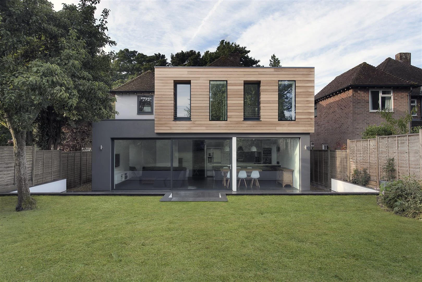 The Medic’s House is a two story rear extension and renovation project, commissioned by two Winchester based Doctors upon the arrival of their new baby daughter. The need for additional family space meant that the client’s existing 1950’s three bed house desperately needed extending. The brief called for two additional bedrooms upstairs and a large open-plan family space with light, views and access to the beautiful garden at ground floor. AR Design Studio’s solution was to create a large charcoal grey living box at ground level with a full height glazed opening elevation to the garden. A timber clad sleeping pod is perched above at first floor level providing the additional bedrooms. At ground floor level the extension contains a utility, WC, kitchen, dining room and lounge area, fitted with three large eco-friendly sliding glass panels creating an uninterrupted view of the garden. The flush threshold and continuous floor surface enhance this connection with the garden by allowing the internal space to flow seamlessly out into it on warmer days. The walls are constructed from super insulated block and oversized insulated cavities ensuring a very thermally efficient envelope. Large opaque glass panels to the sides allow etch light to enter deep into the plan of the space. The structure is hidden in strategically placed fins that suggest living zones within the open-plan space. Upstairs, the western red cedar clad addition consists of a generous master suite with a separate dressing area and one other additional bedroom. This upper box is also fabricated in timber, allowing for a light weight structure that reduces the need for unsightly columns beneath. The construction contains over 250mm of insulation which AR felt was important at the upper level. This approach to construction was also carried through into the over insulated single-ply roof. The fenestration was resolved as a series of verticals that celebrate the depth of the walls with a combination of recessed and flush frameless windows. The overall composition was influenced by the ancient Greek theory of the ‘Golden Section’ in order to provide a well-balanced and proportioned rear elevation.