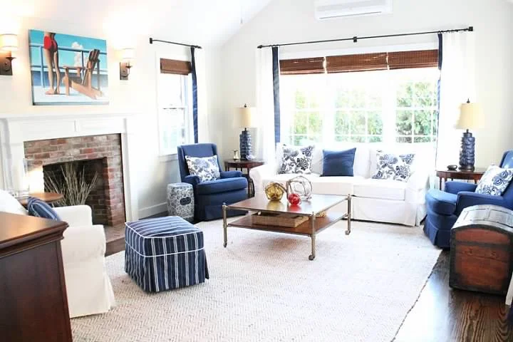 Above, a brass and maple Barclay Butera coffee table is adorned with Homegoods accents and Ikea's budget ottomans compliment custom upholstered navy chairs.