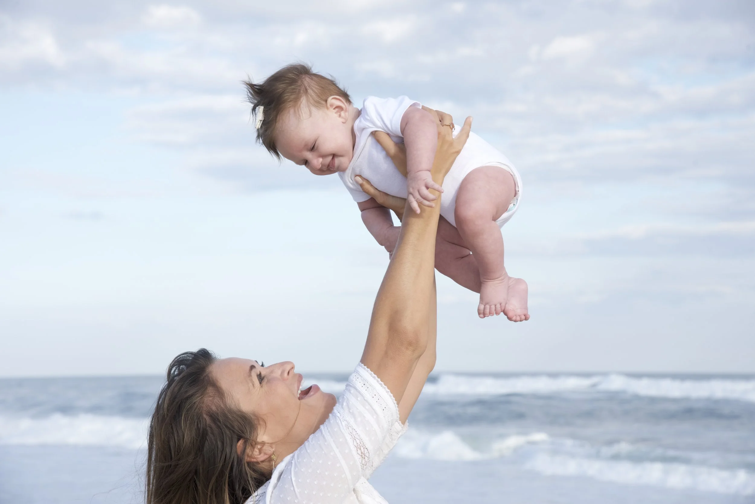 mother lifts baby n the air at a Hampton beach photo session with lifestyle photographer