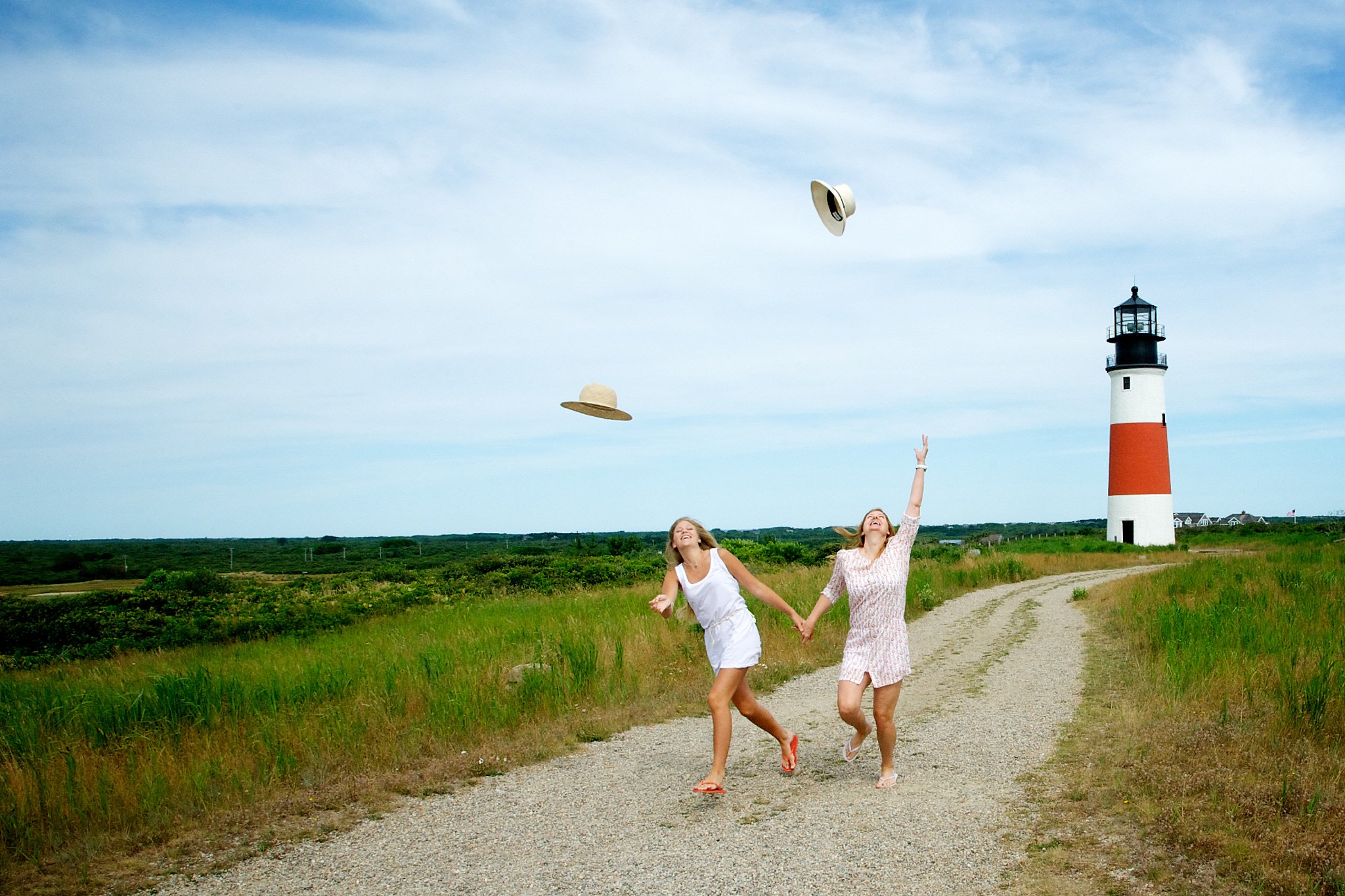 Pamela Einarsen, Nantucket family photographer, captures a mother and daughter laughing as they toss their sunhats in the air near Sconset Lighthouse on a vacation photo session.