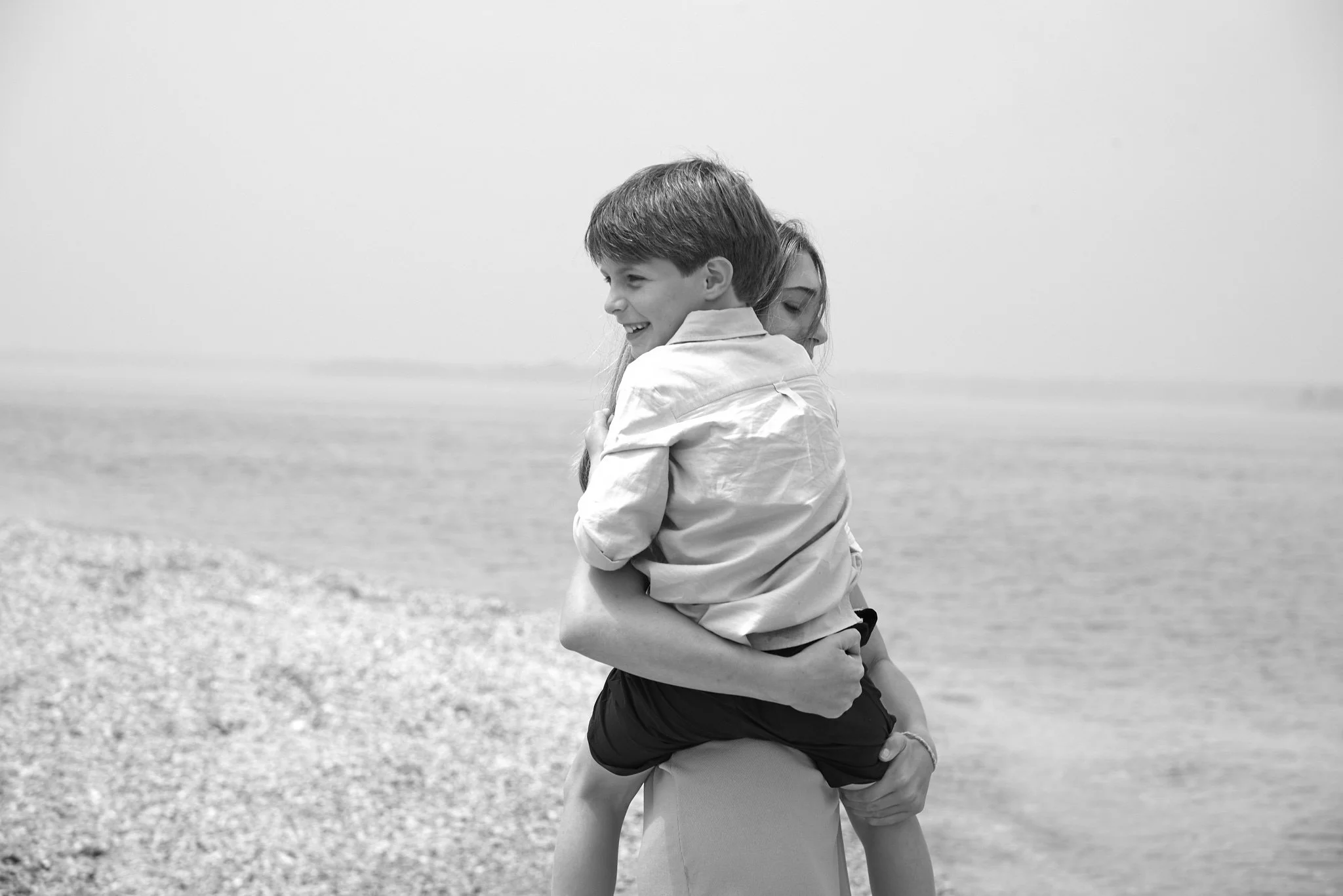 Mom hold her son in B&amp;W photo by the beach.