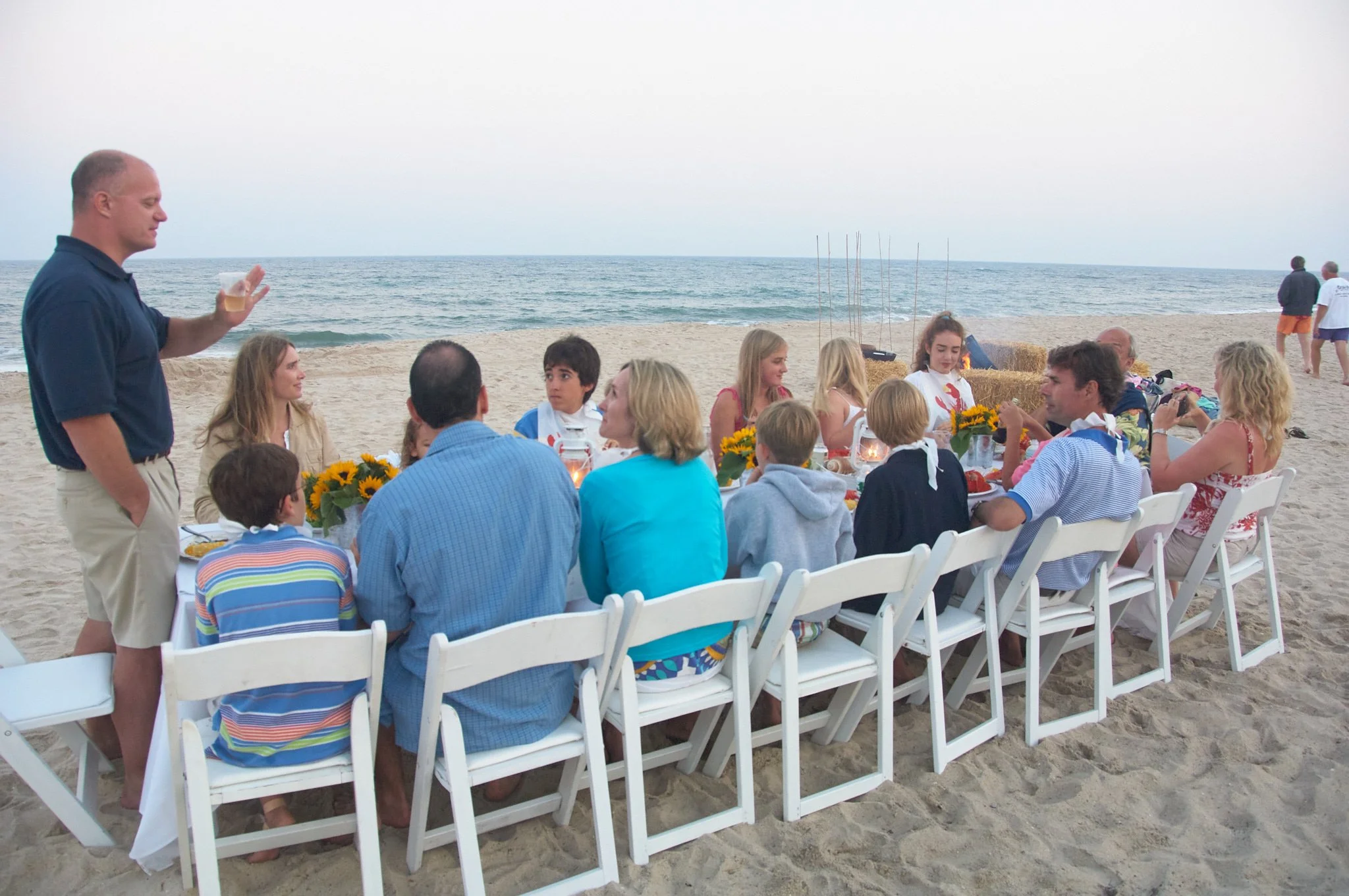 Man toasts his family at a lobster bake on a Hampton beach by extended family photographer Pamela Einarsen.
