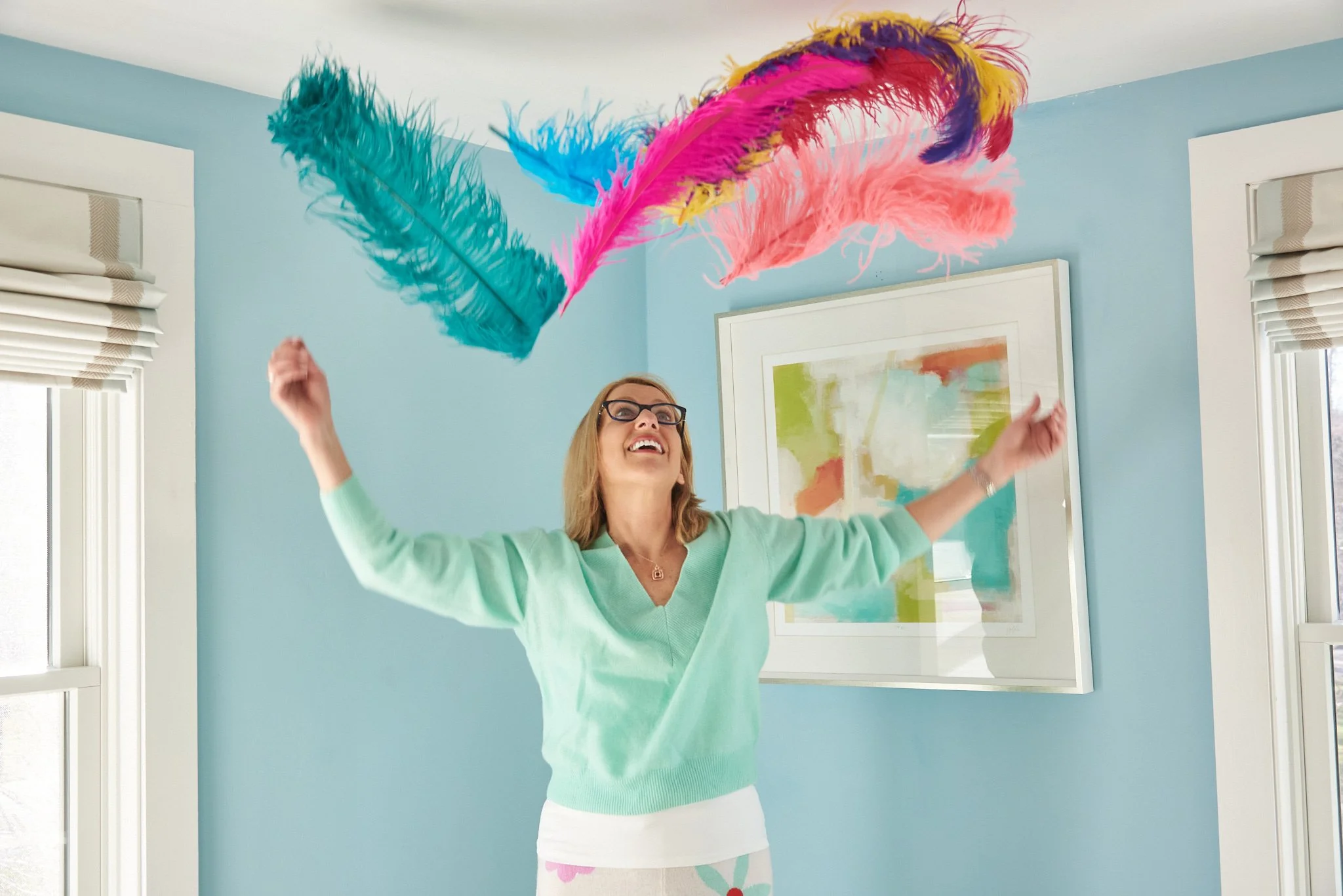 Woman smiles at feathers thrown in the air at her Ridgefield, CT home during a brand session with lifestyle photographer Pamela Einarsen. 