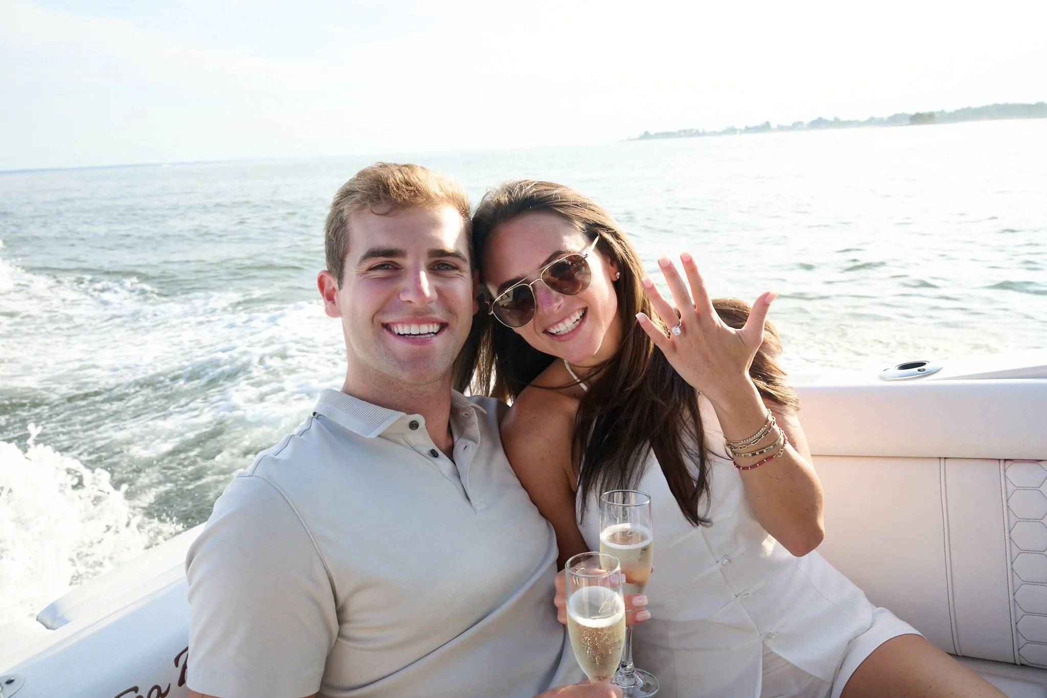 Couple show engagement ring as they drink champagne on a boat after a proposal on Green ledge Lighthouse in Rowayton CT  by photographer Pamela Einarsen.