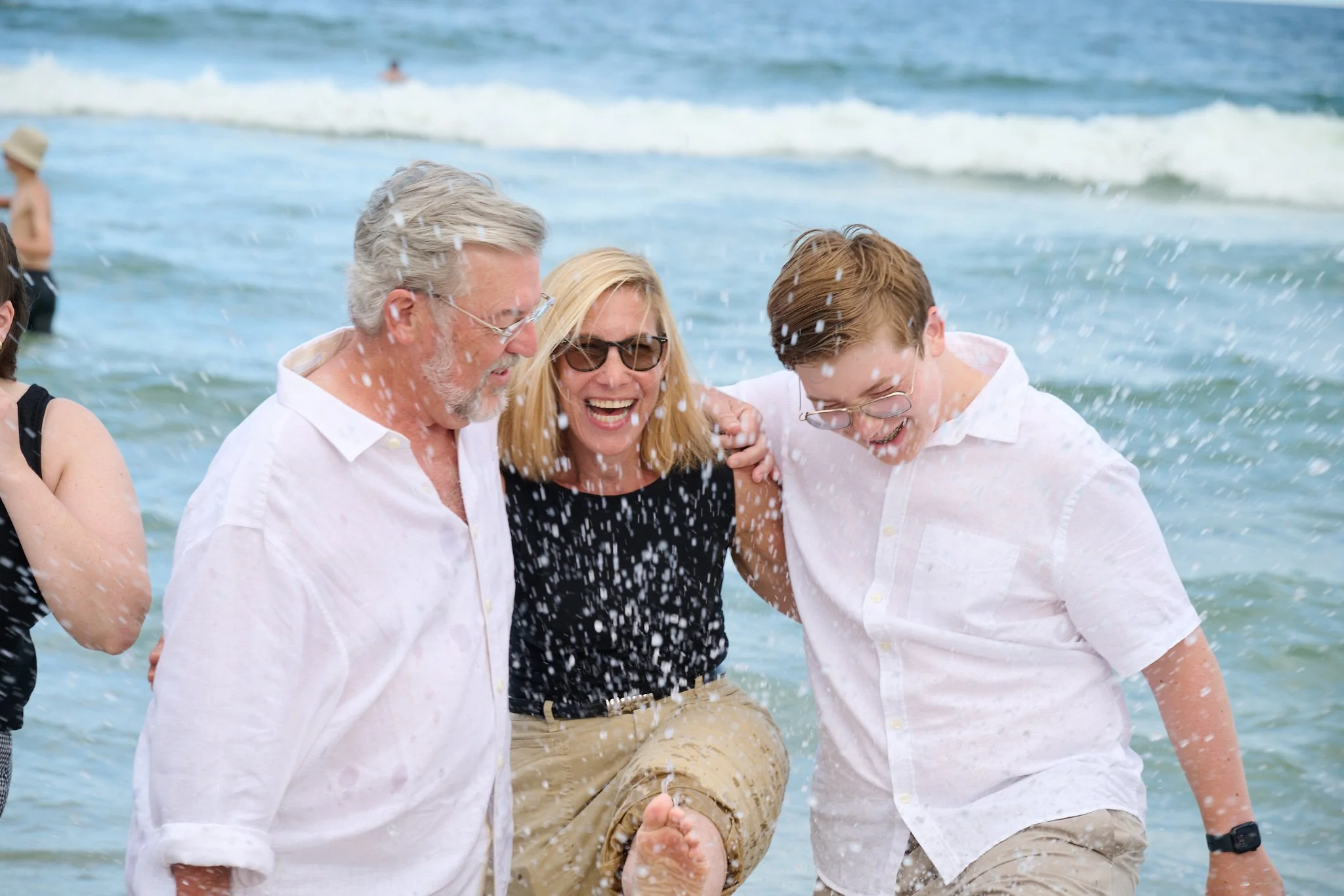 Woman laughs with her husband and son as they splash in the ocean on the Jersey Shore with family photographer Pamela Einarsen. 