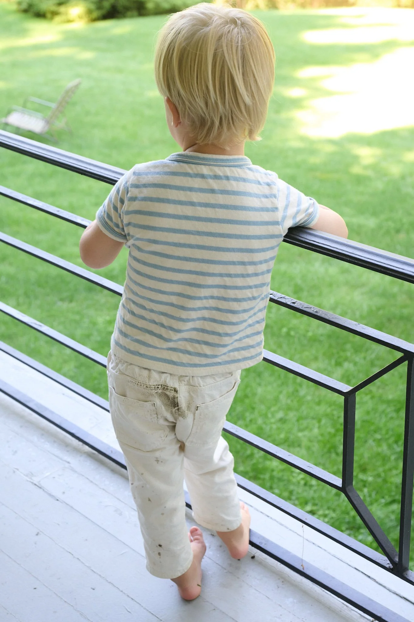 Candid moment of toddler with muddy pants looking out over a Westport CT yard by lifestyle photographer Pamela Einarsen. 