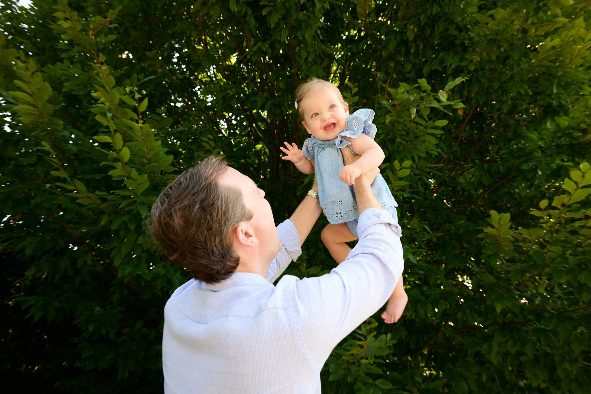 Dad lifts baby into the air in Westport, CT backyard by lifestyle photographer Pamela Einarsen.