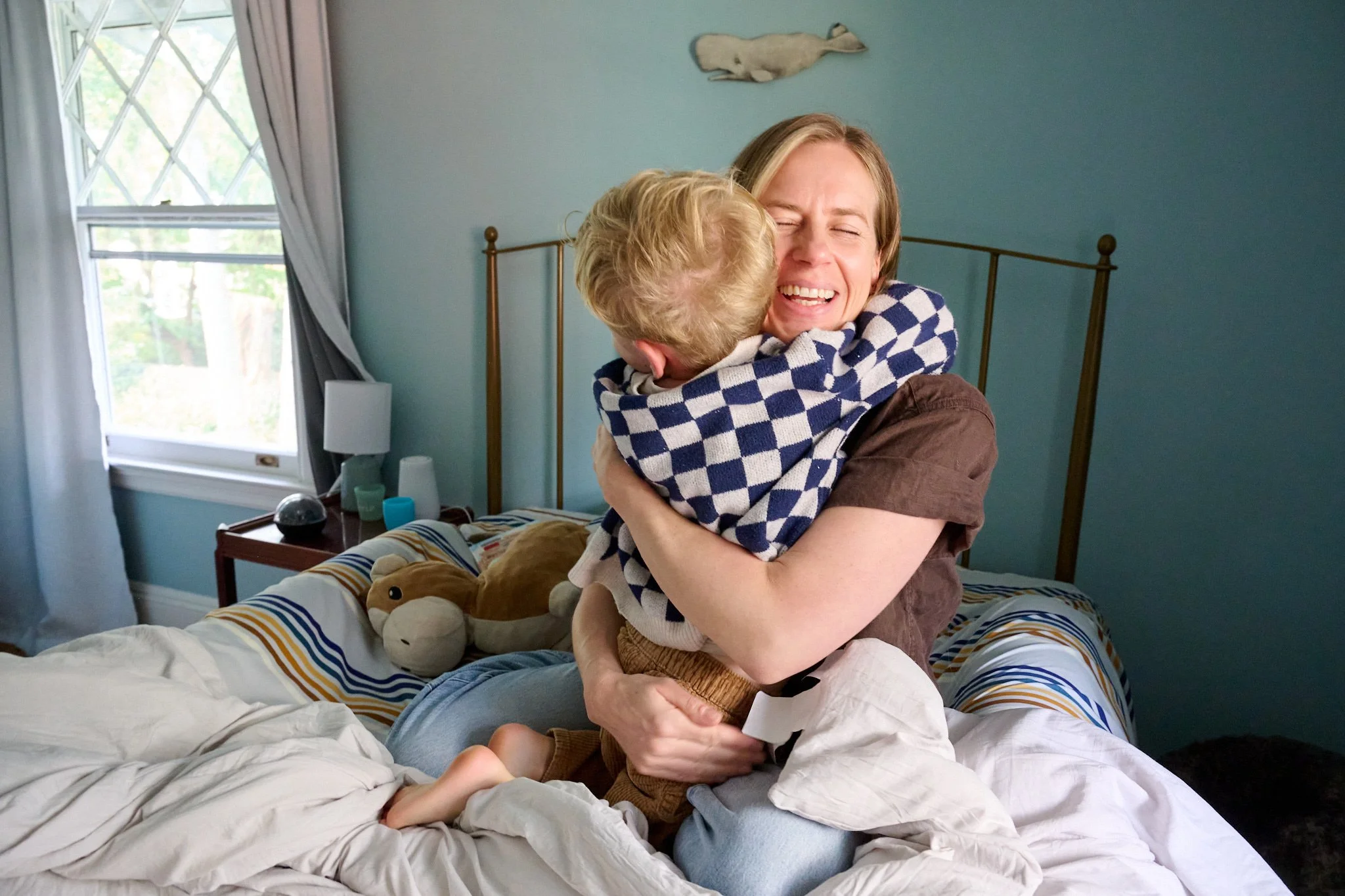 Mom smiles and hugs young boy on bed in West Hartford, CT house by lifestyle photographer Pamela Einarsen, 