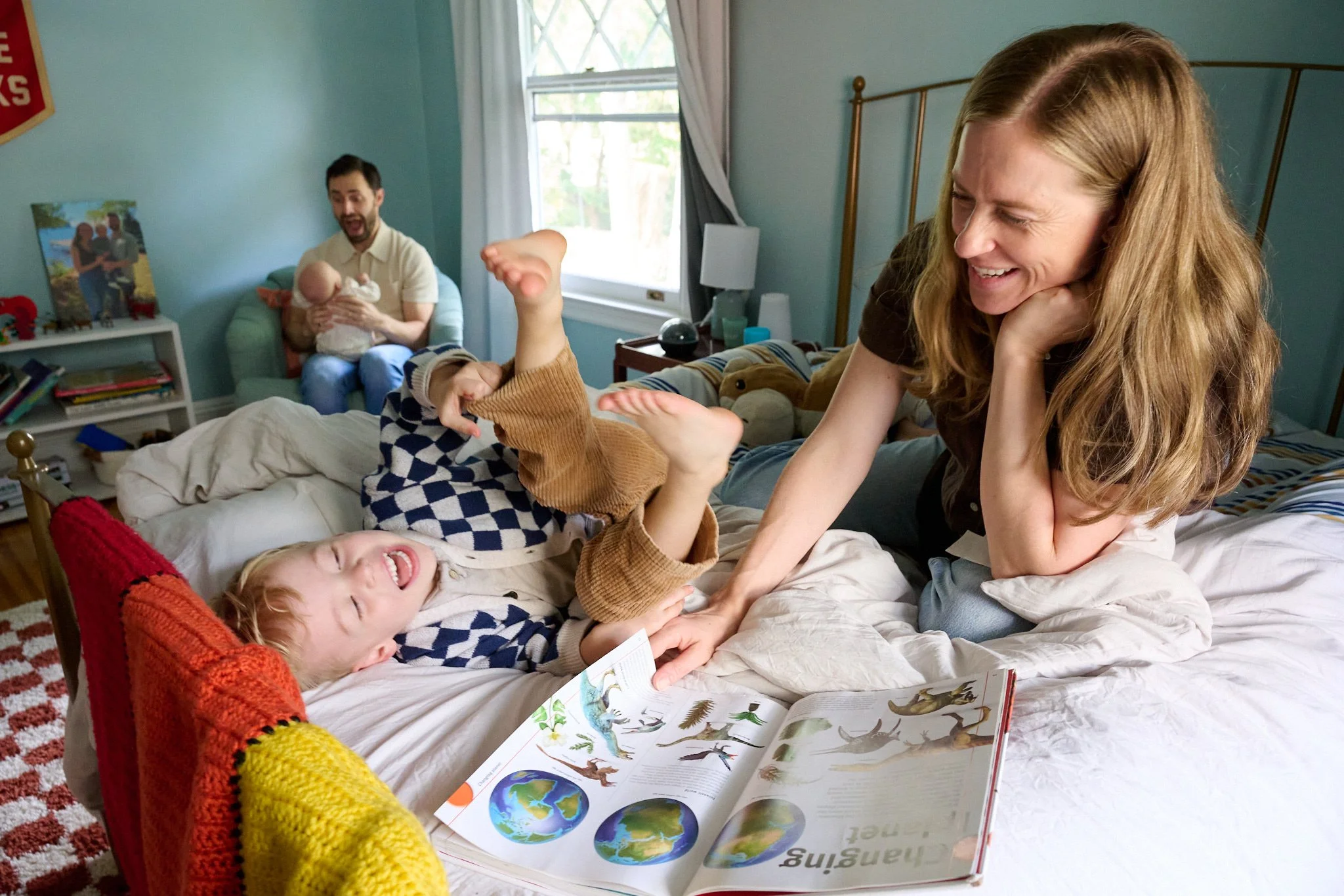 Mother and son laugh on bed as father and newborn baby smile in background in West Hartford home with family photographer Pamela Einarsen.