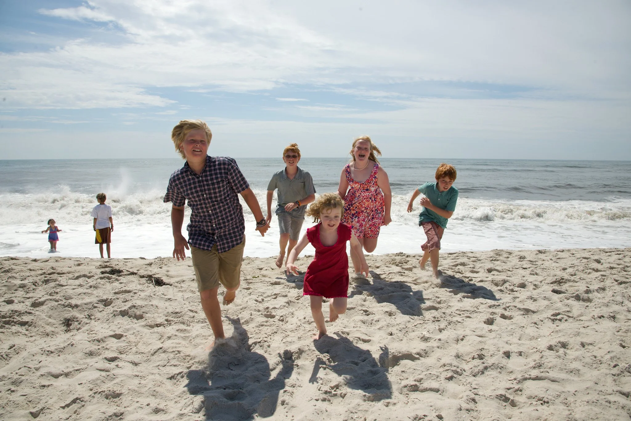 Children run on Fire Island beach with waves in a lifestyle session with photographer