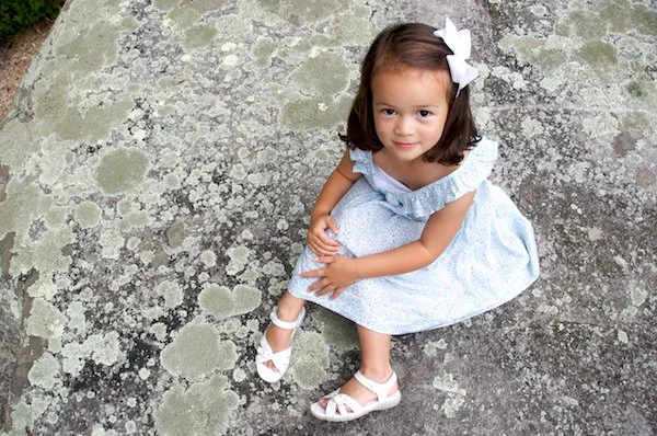 Girl smiies at family photographer on a rock in Ridgefield