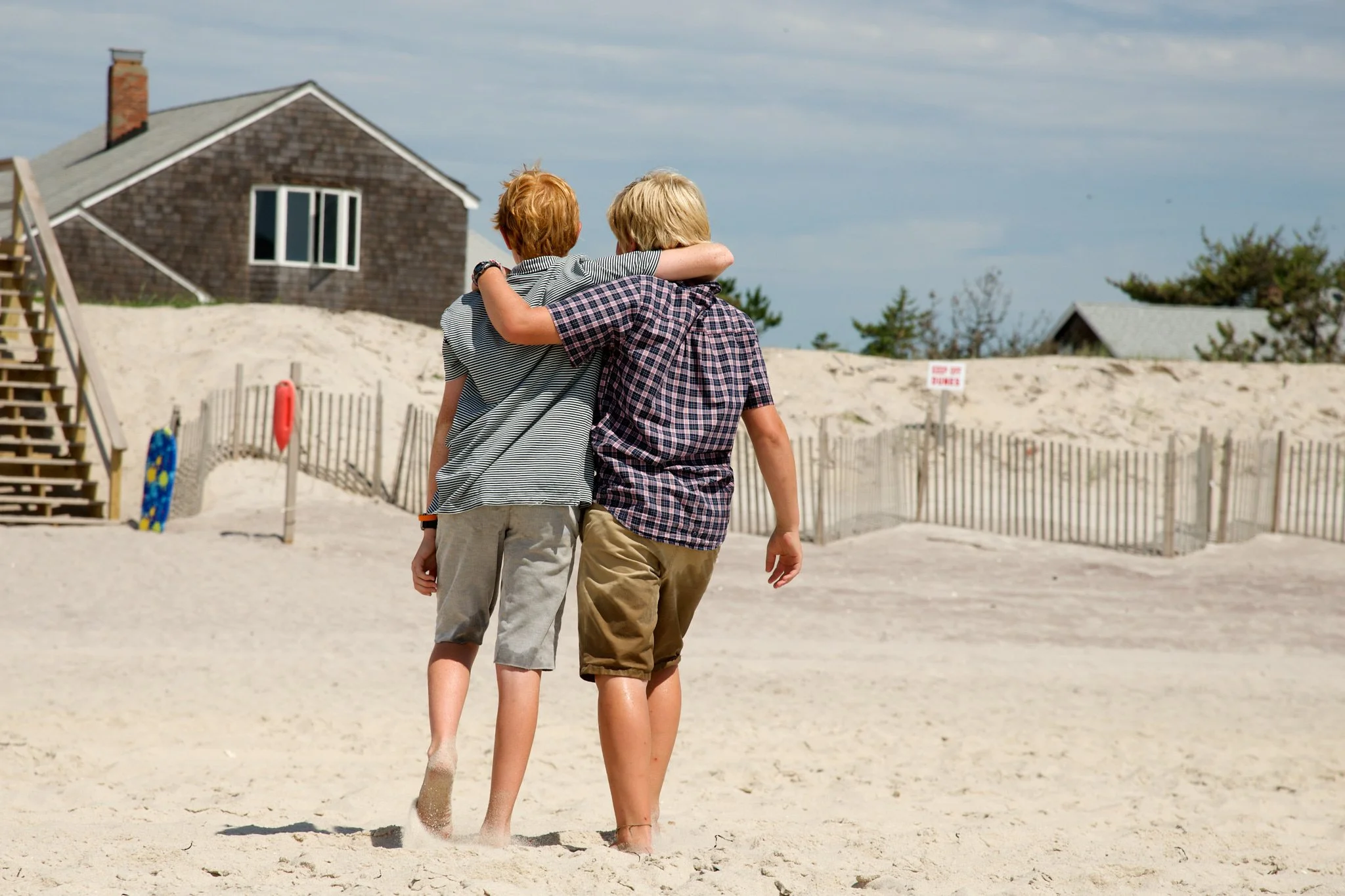 Boys walk with arms around each other on a Fire Island beach with photographer
