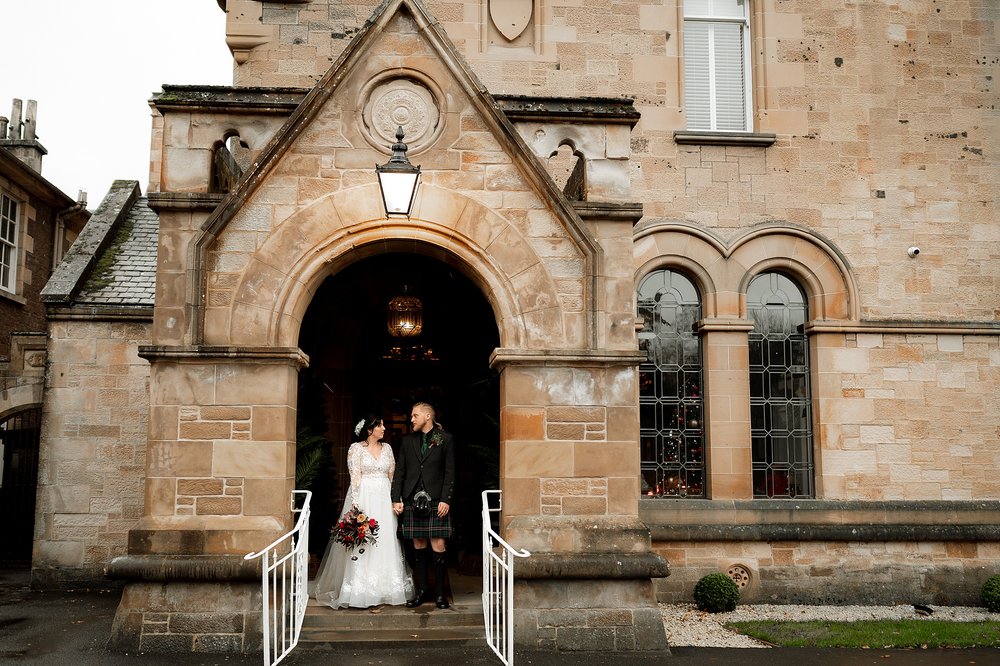 exterior outside view of cornhill castle showing the bride and groom standing in the arched doorway following their wedding ceremony in biggar in lanarkshire