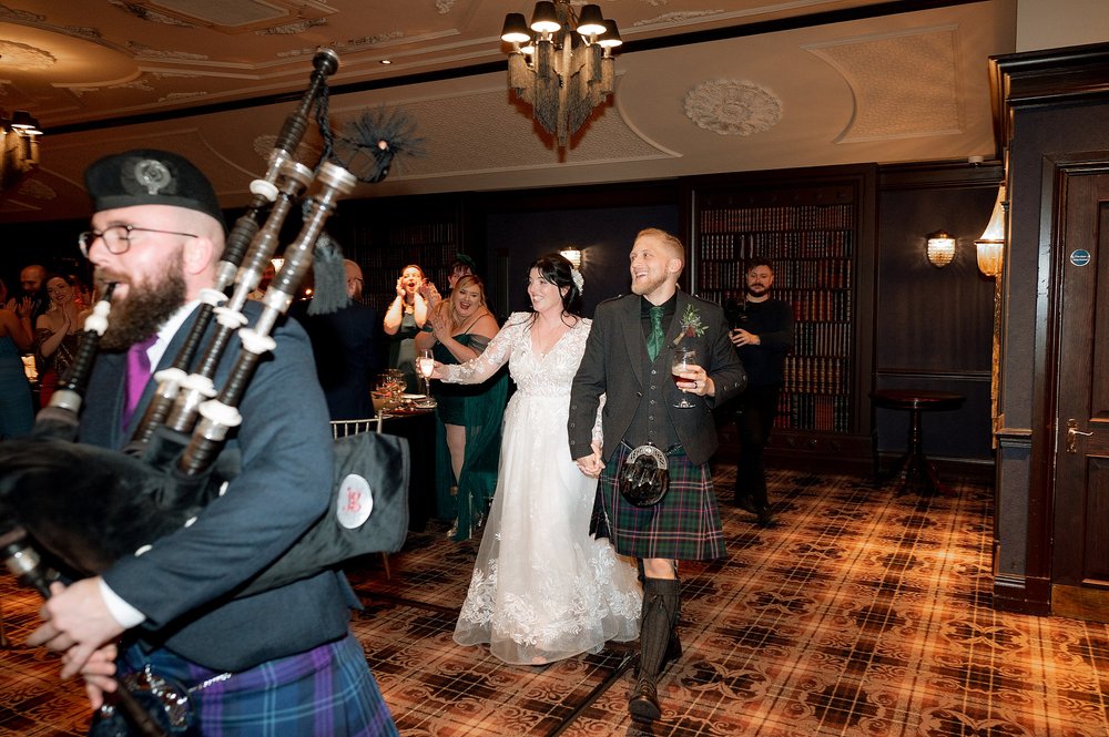 the bride and groom enter led by a piper for their wedding reception organised by an american destination wedding planner in glasgow
